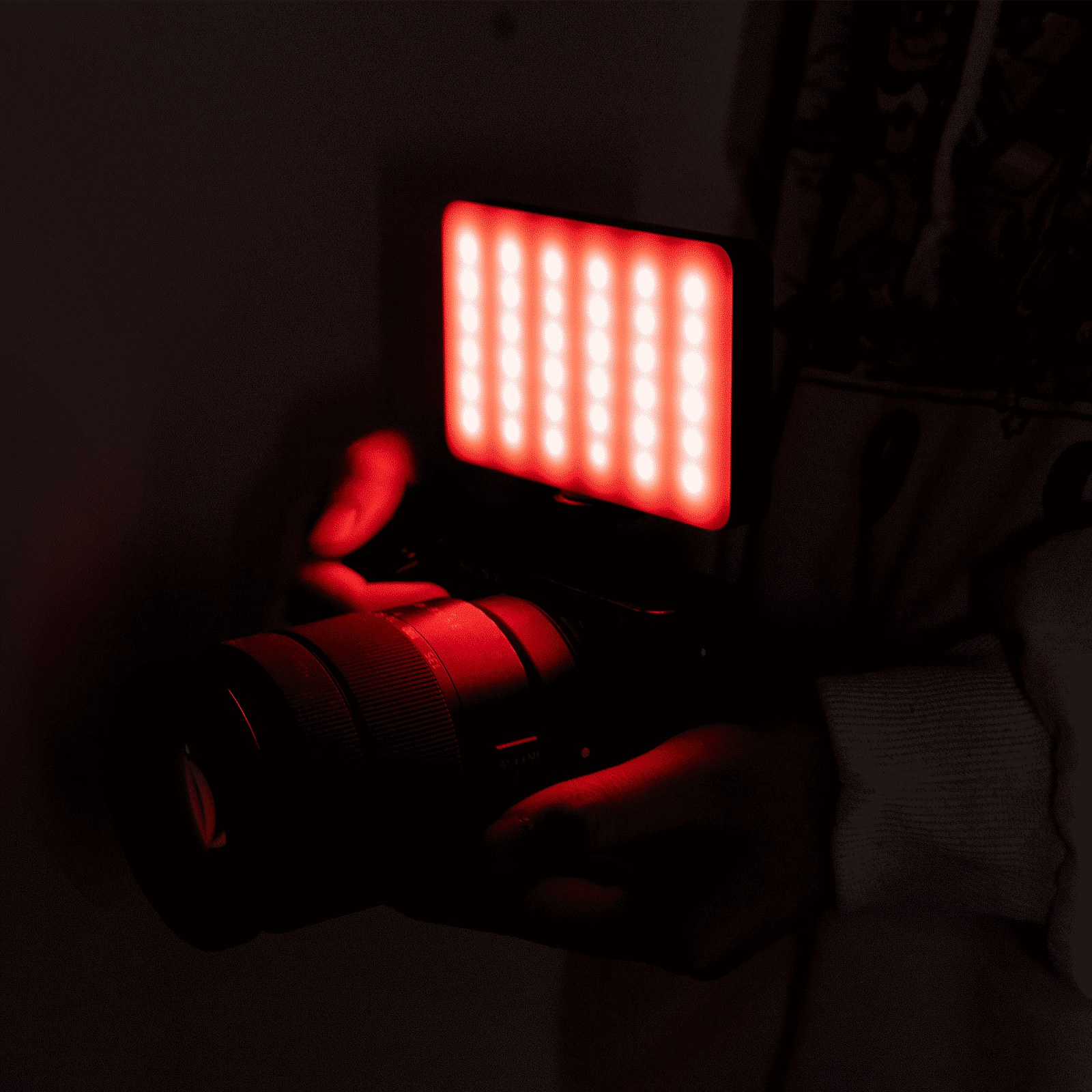 A camera with an attached glowing red LED panel is held in a dark environment.