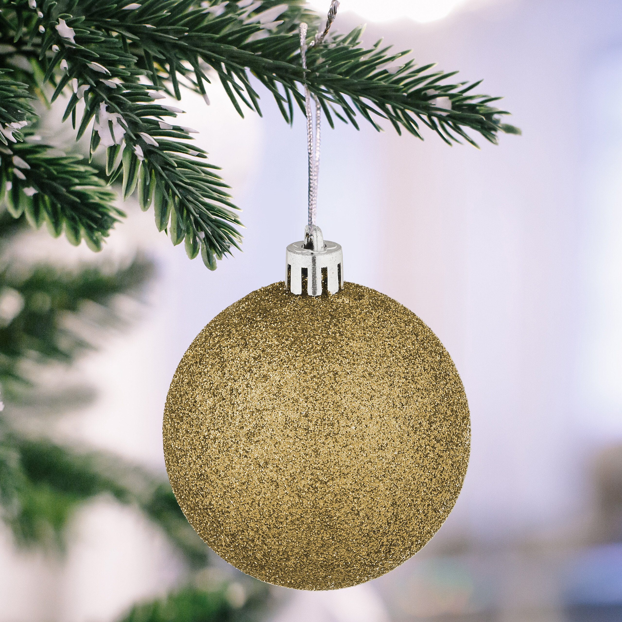 Eine glitzernde goldene Weihnachtskugel hängt an einem verschneiten Tannenzweig.