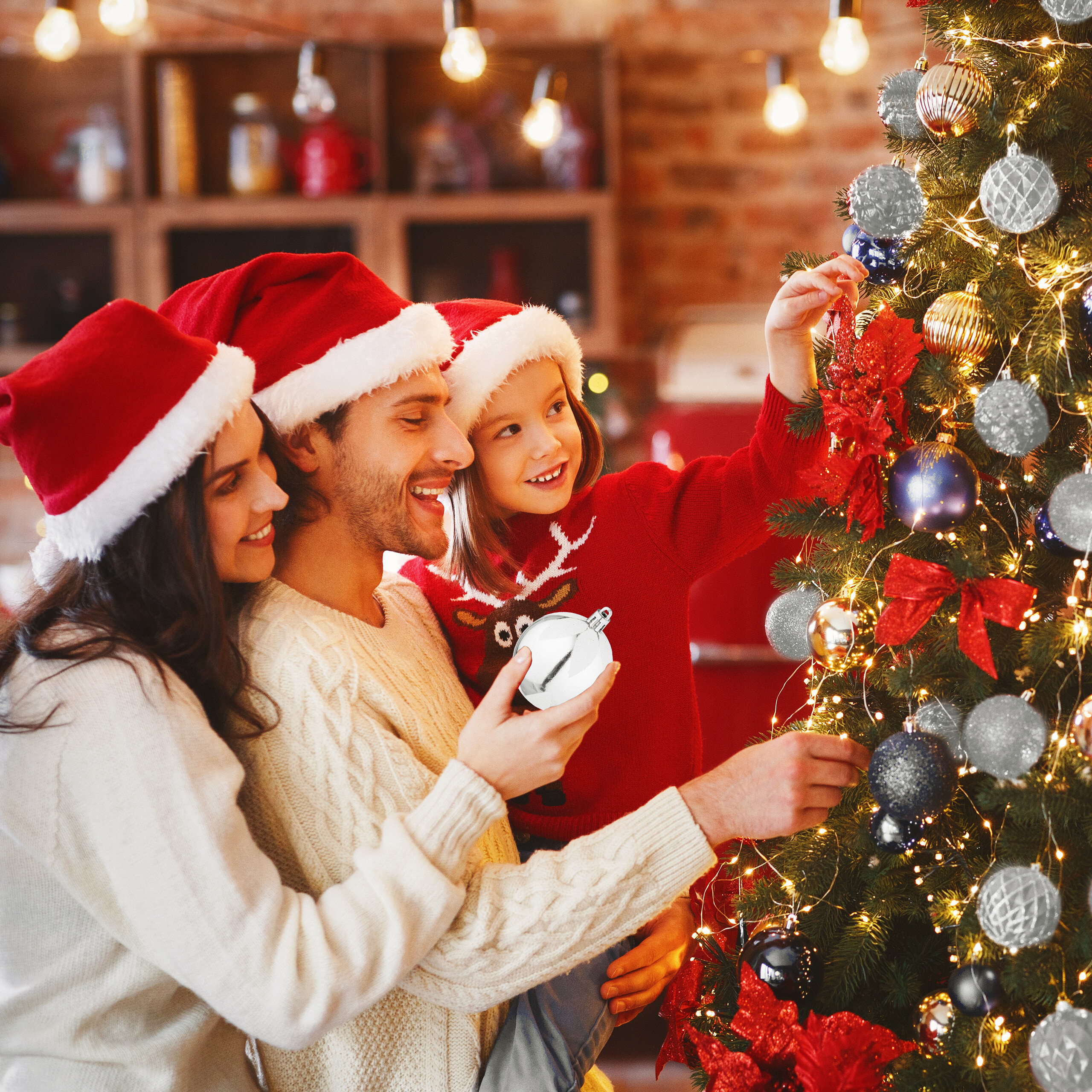 Familie mit Weihnachtsmützen dekoriert gemeinsam einen Weihnachtsbaum in einem gemütlichen Raum.