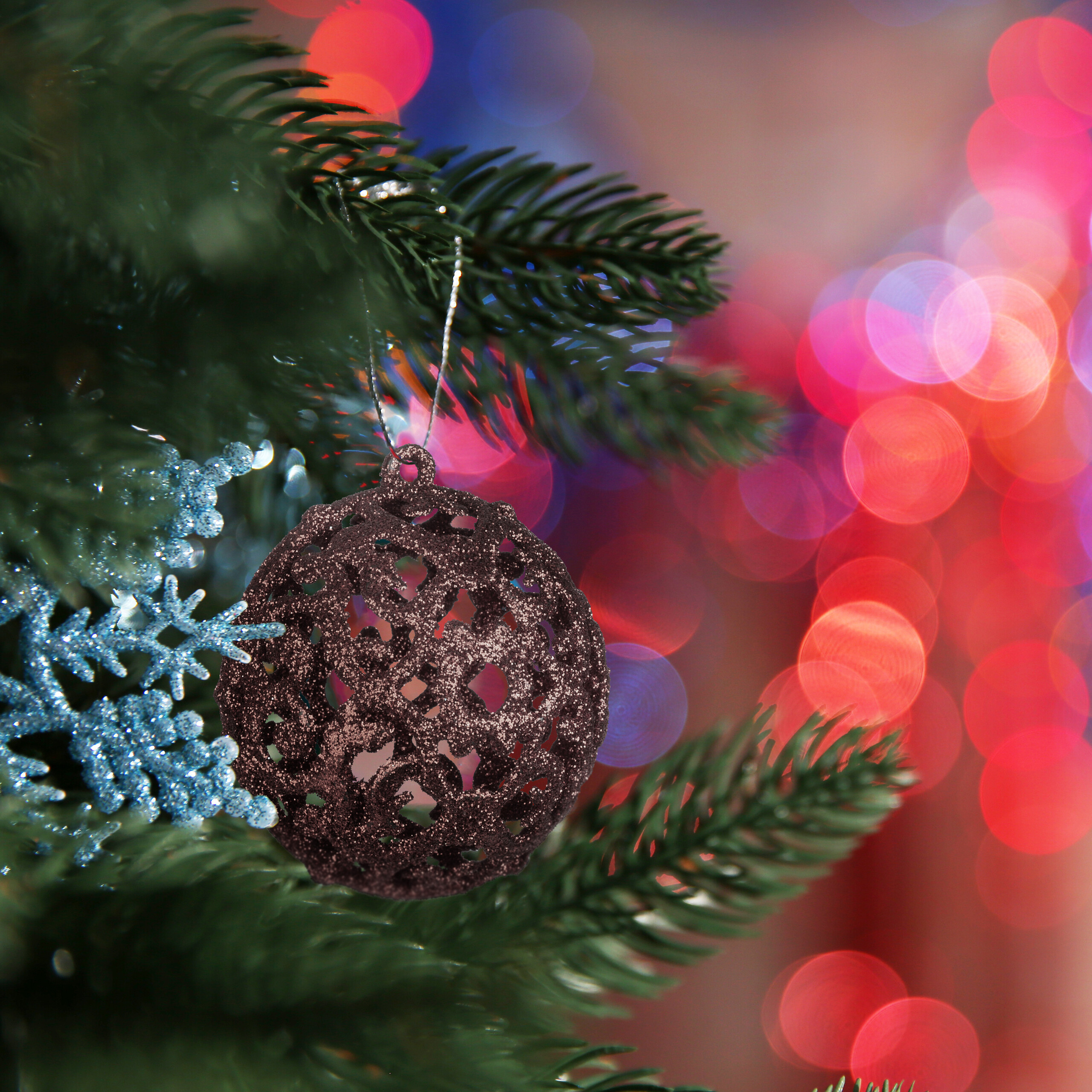 Eine dunkelbraune Kugel und blaue Schneeflocken hängen an einem grünen Weihnachtsbaum vor verschwommenem Hintergrund.