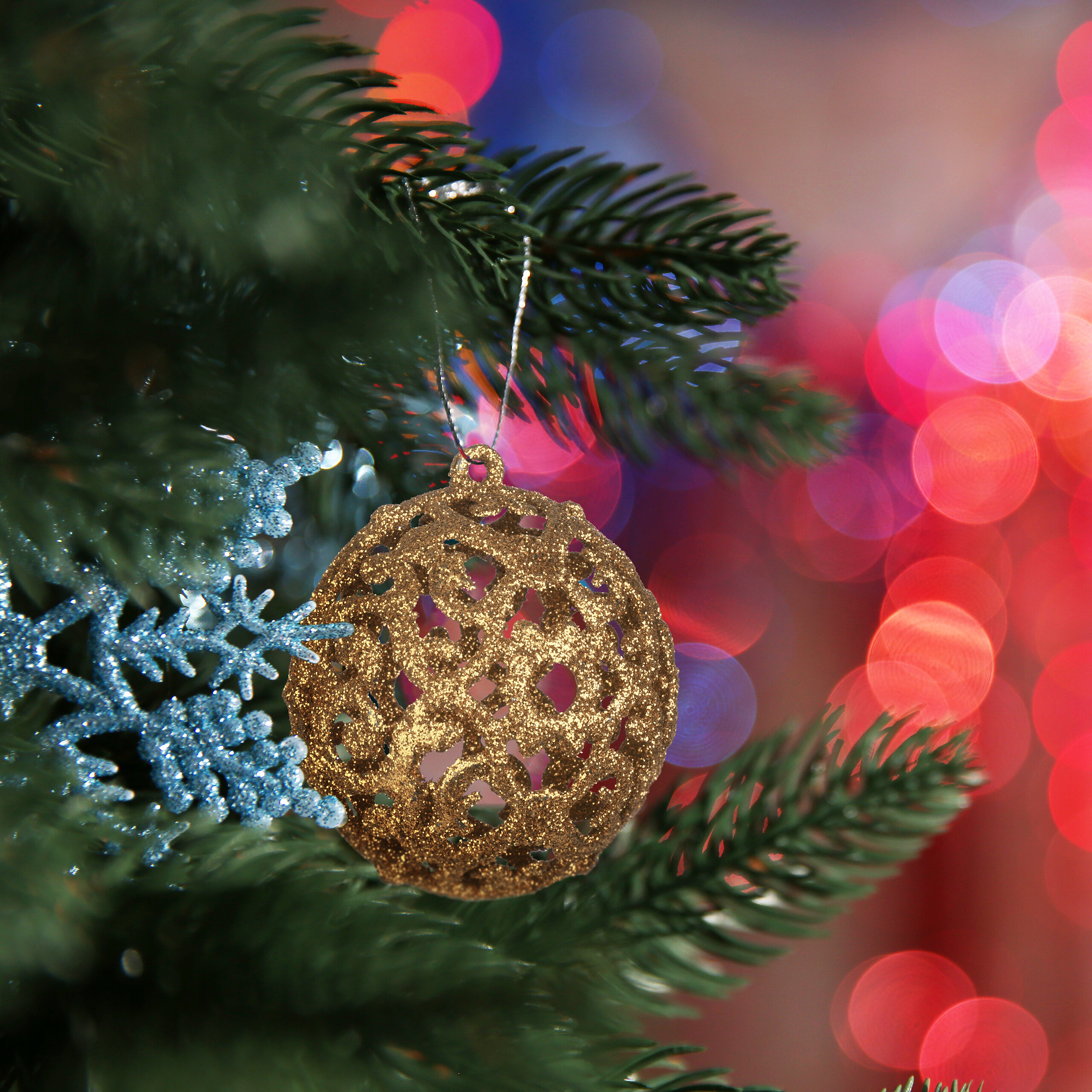 Eine glitzernde goldene Weihnachtskugel und blaue Schneeflocken an einem grünen Baum vor verschwommenem Hintergrund.