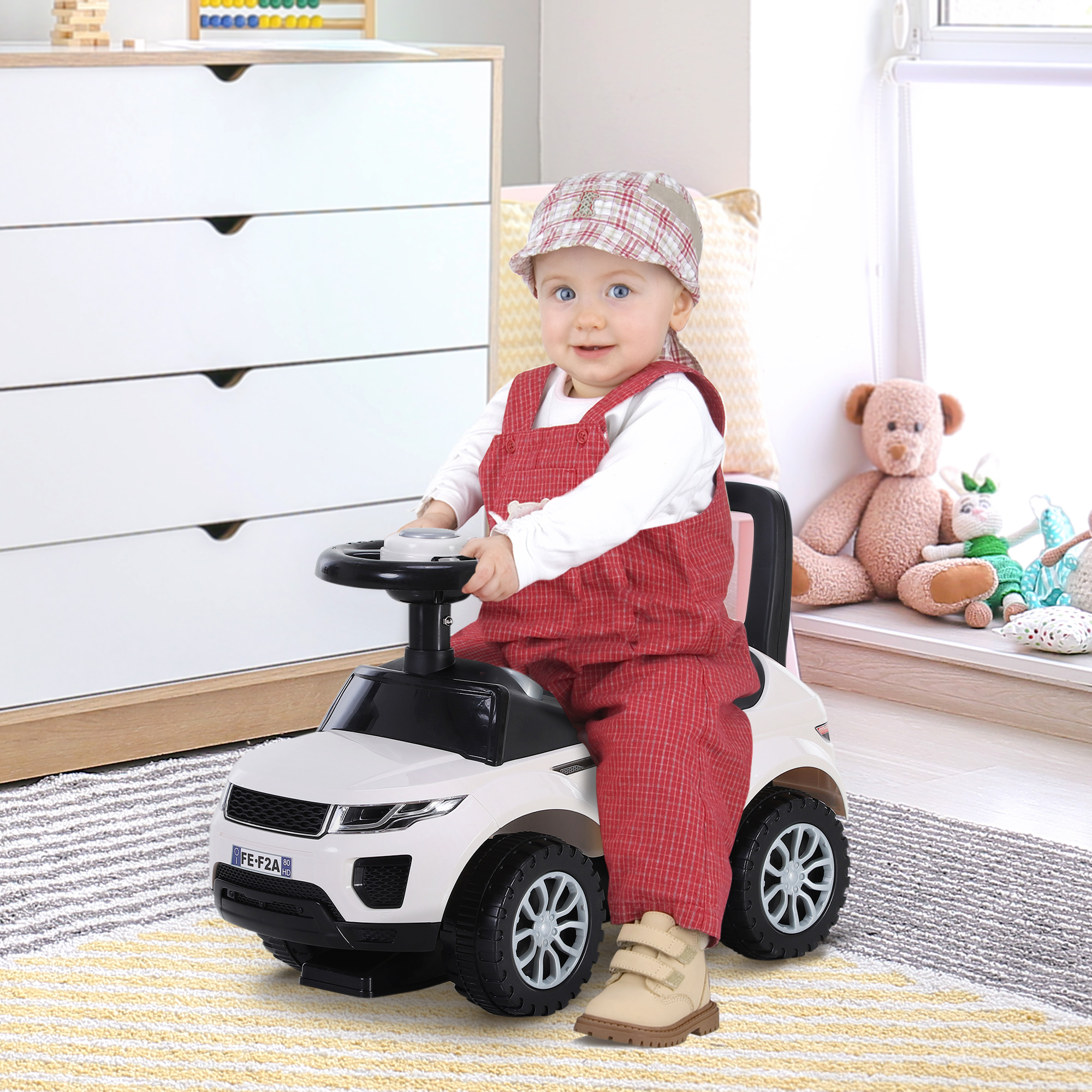 Bambino con salopette rossa sorride seduto su un'auto giocattolo bianca in una stanza.