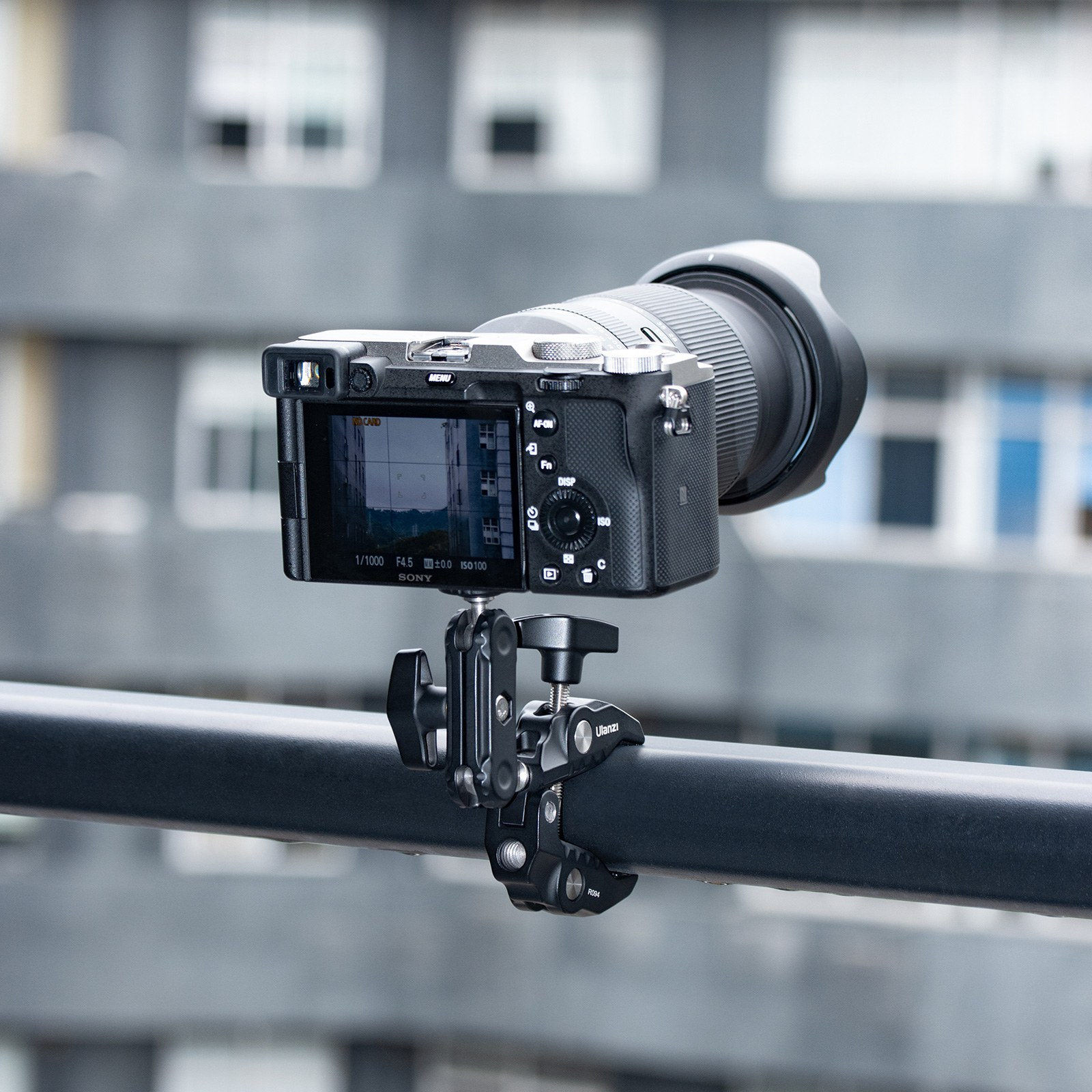 Una fotocamera mirrorless Sony montata su una ringhiera nera con un morsetto, con un edificio sfocato.