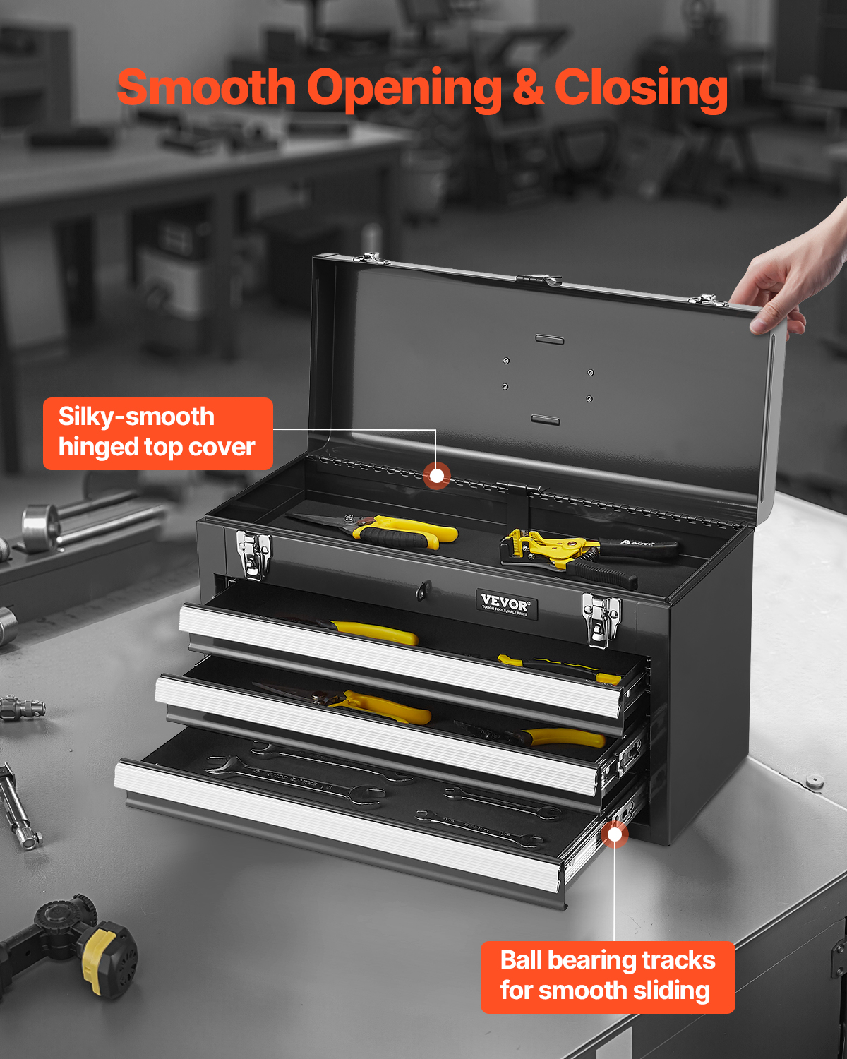 Una caja de herramientas de metal negro con tres cajones y tapa abierta sobre un banco de trabajo.