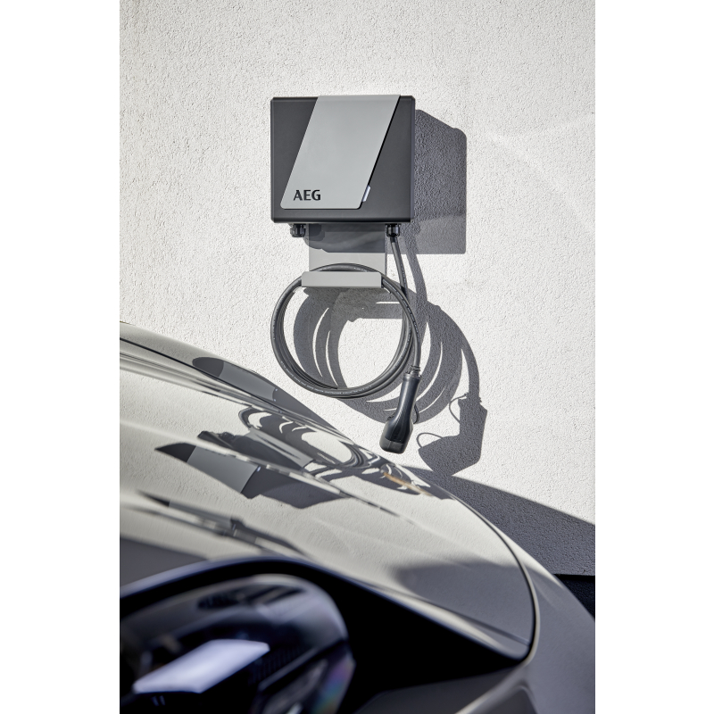 Eine graue und schwarze AEG-Wallbox hängt an einer weißen Wand, mit einem aufgewickelten Kabel über einem Auto.