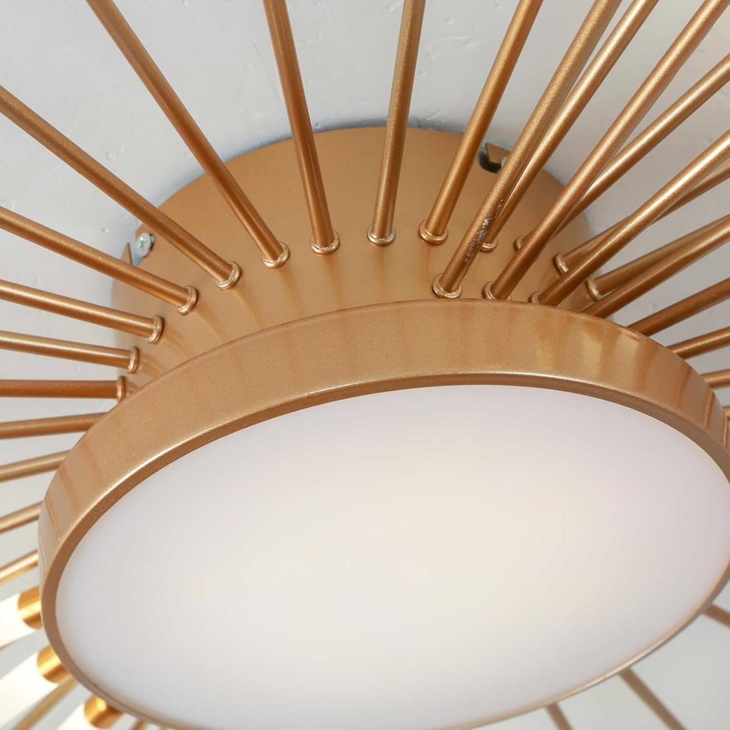 Eine moderne goldene Deckenleuchte mit rundem Diffusor und strahlenden Metallstäben an weißer Decke.