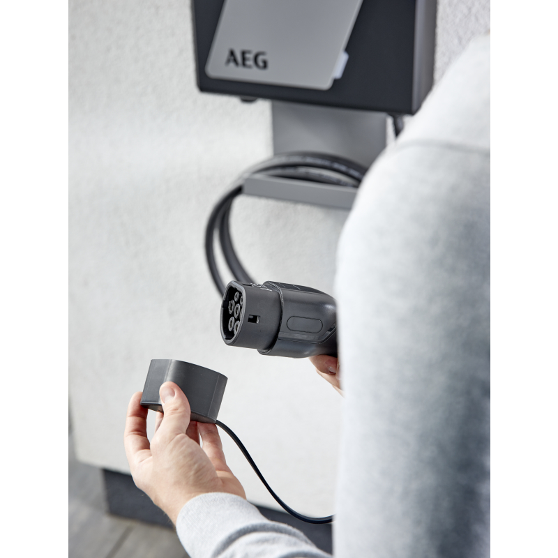 Person hält den Stecker einer grauen AEG-Wand-Ladestation bereit.