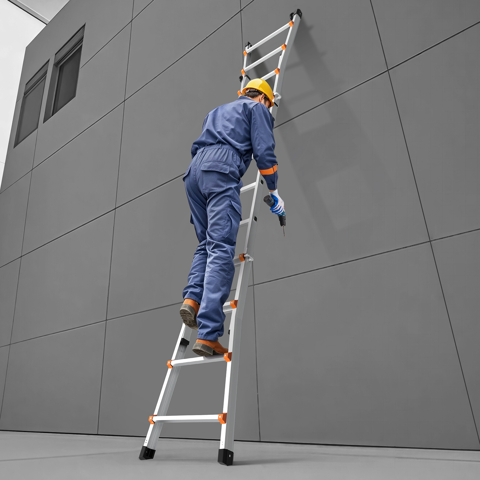 Un trabajador con mono azul y casco amarillo sube por una escalera extensible gris contra una pared.