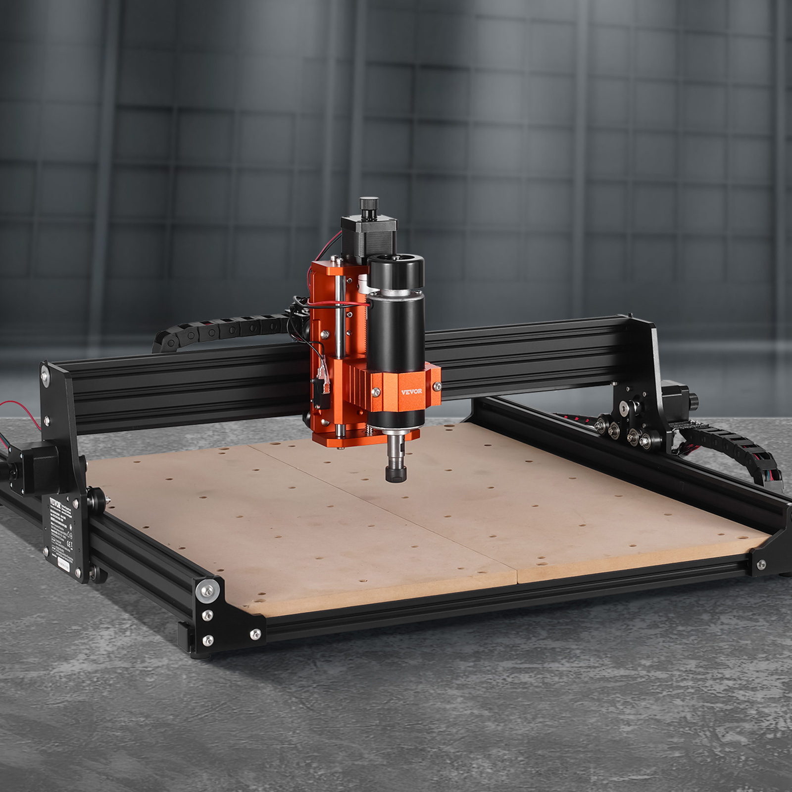Una máquina enrutadora CNC negra y naranja se encuentra en un banco de trabajo sobre un fondo gris.