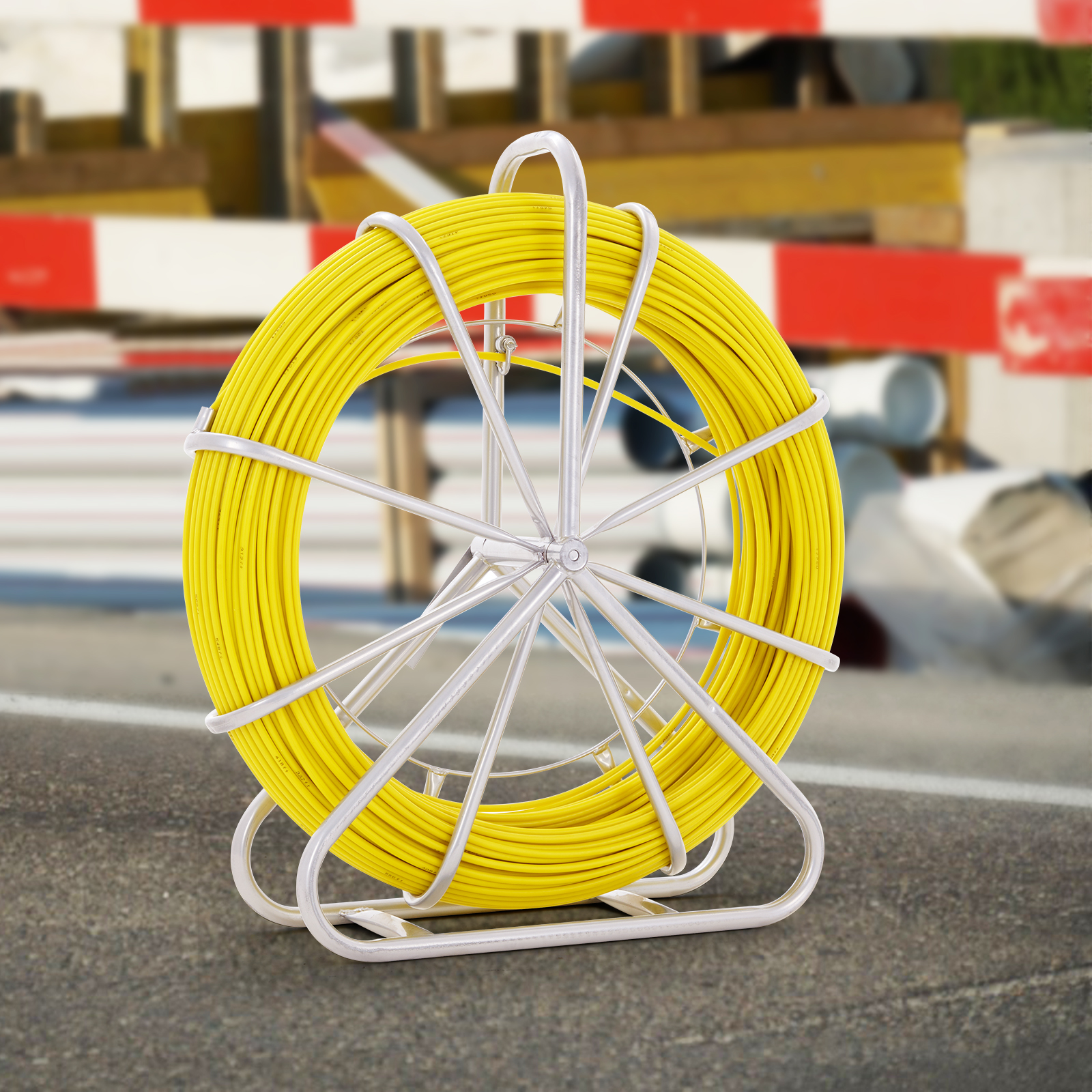 Un gran carrete de cable amarillo brillante en un soporte de metal al aire libre, con una barrera roja y blanca al fondo.