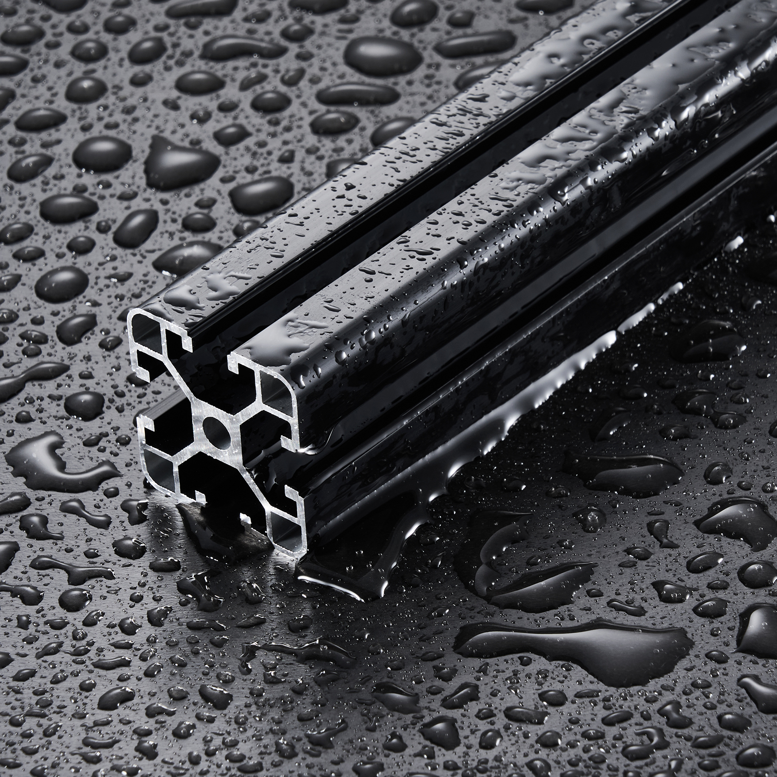 Un perfil de aluminio extruido negro descansa sobre una superficie mojada y reflectante cubierta de gotas.