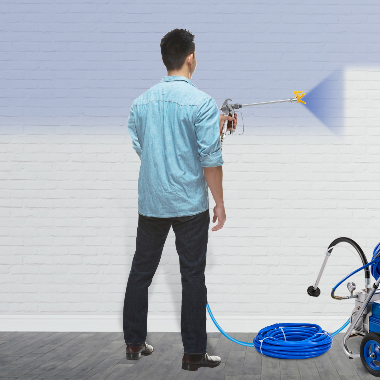 Un hombre con camisa azul y vaqueros oscuros pinta una pared de ladrillo blanco con una máquina azul.