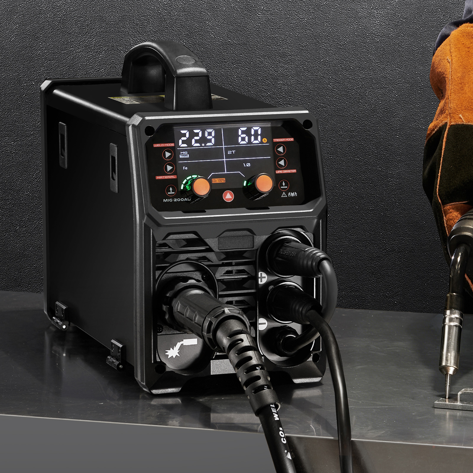 Una máquina de soldar MIG negra sobre una mesa de acero inoxidable, conectada con cables negros gruesos.