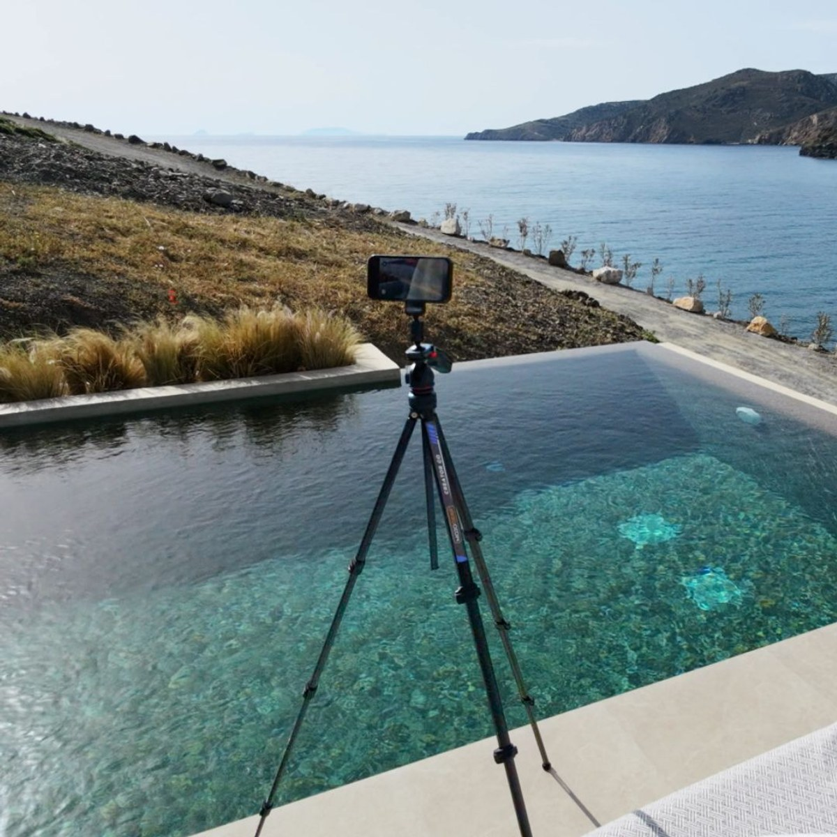 A smartphone on a tripod by a pool edge overlooking the sea.