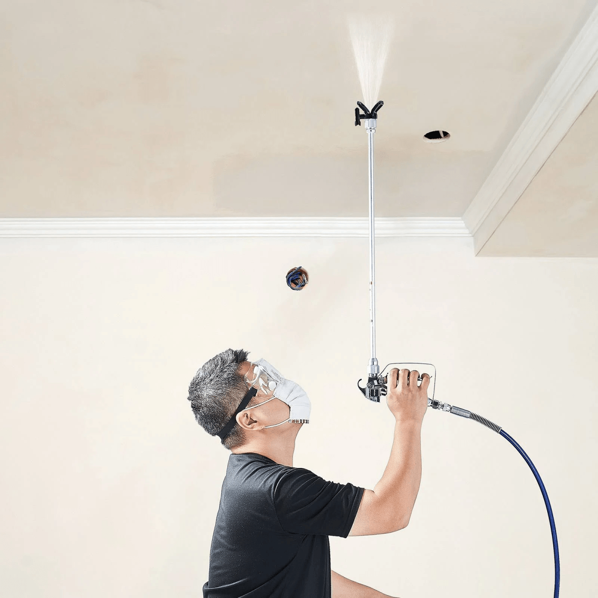 Un trabajador con mascarilla y gafas pulveriza el techo con una pistola de pintura.