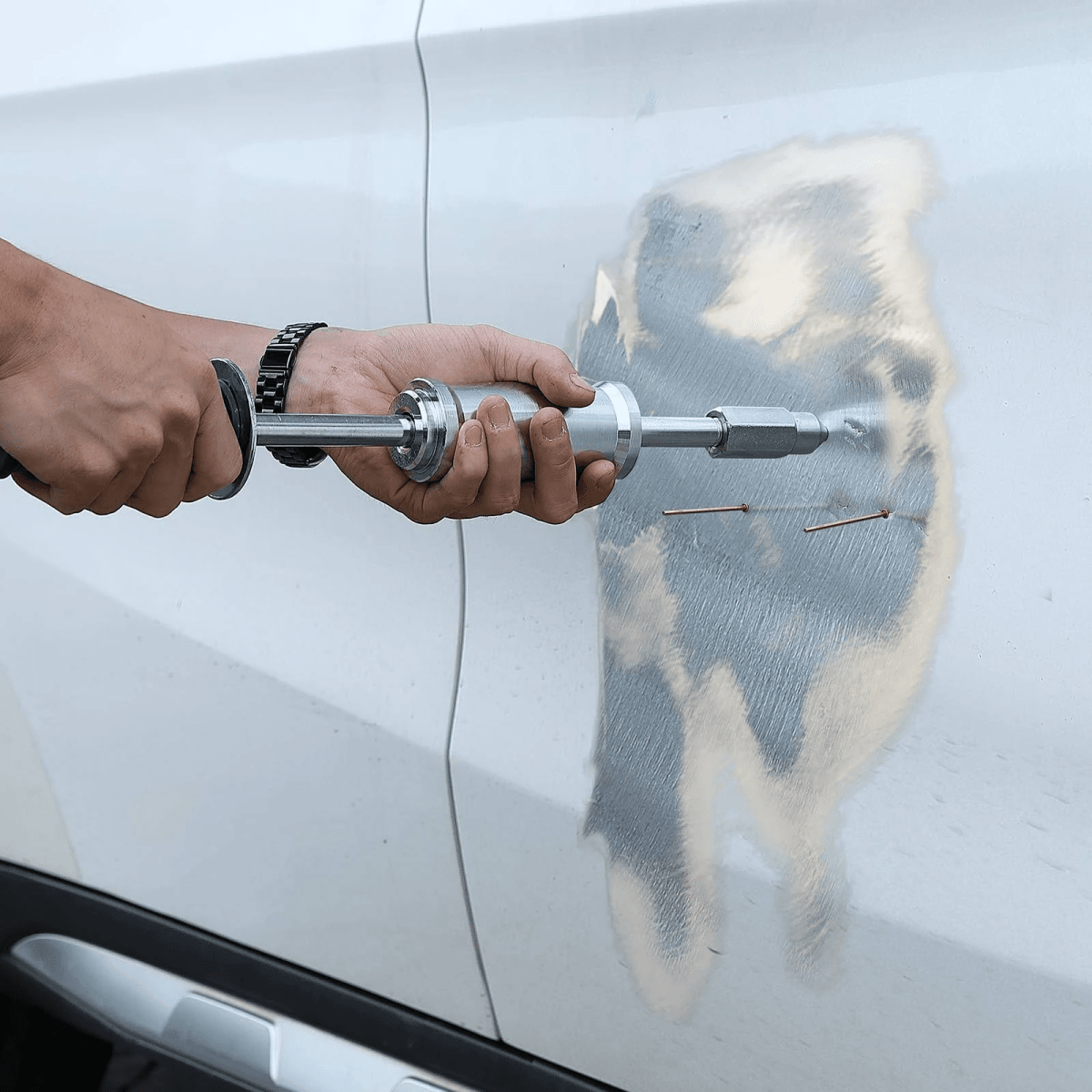Una persona usa un martillo deslizante para sacar un abolladura en una puerta de auto blanca.