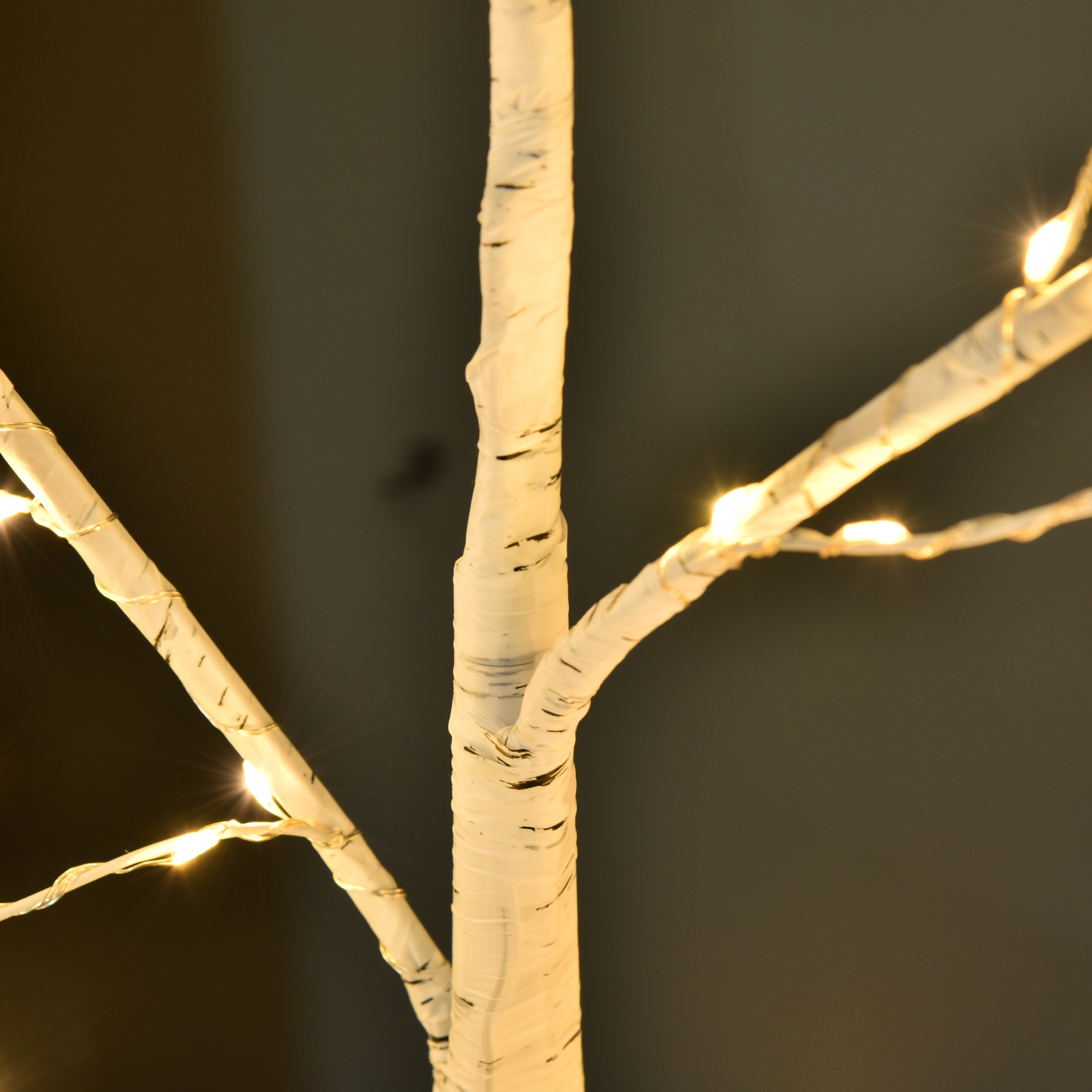 Primer plano de un árbol de ramas decorativo blanco envuelto con luces cálidas sobre fondo oscuro.