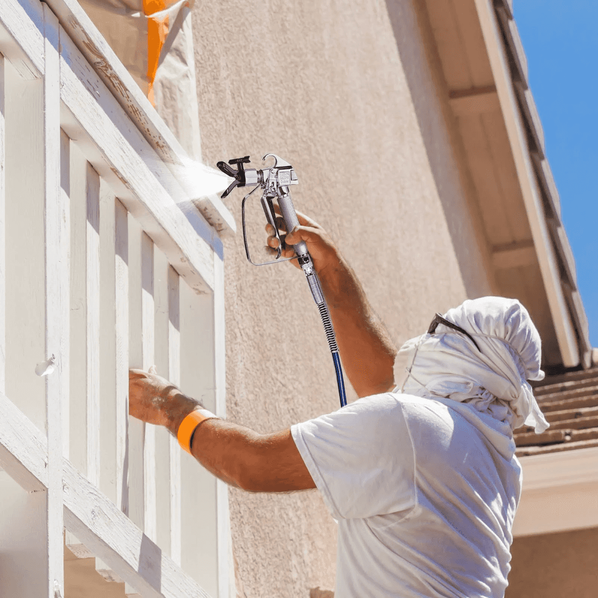 Un trabajador con equipo de protección blanco pinta una barandilla de madera blanca en una pared.