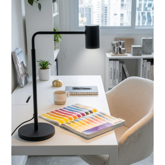 Un escritorio blanco con una lámpara negra, un muestrario de colores abierto, una taza y una silla.