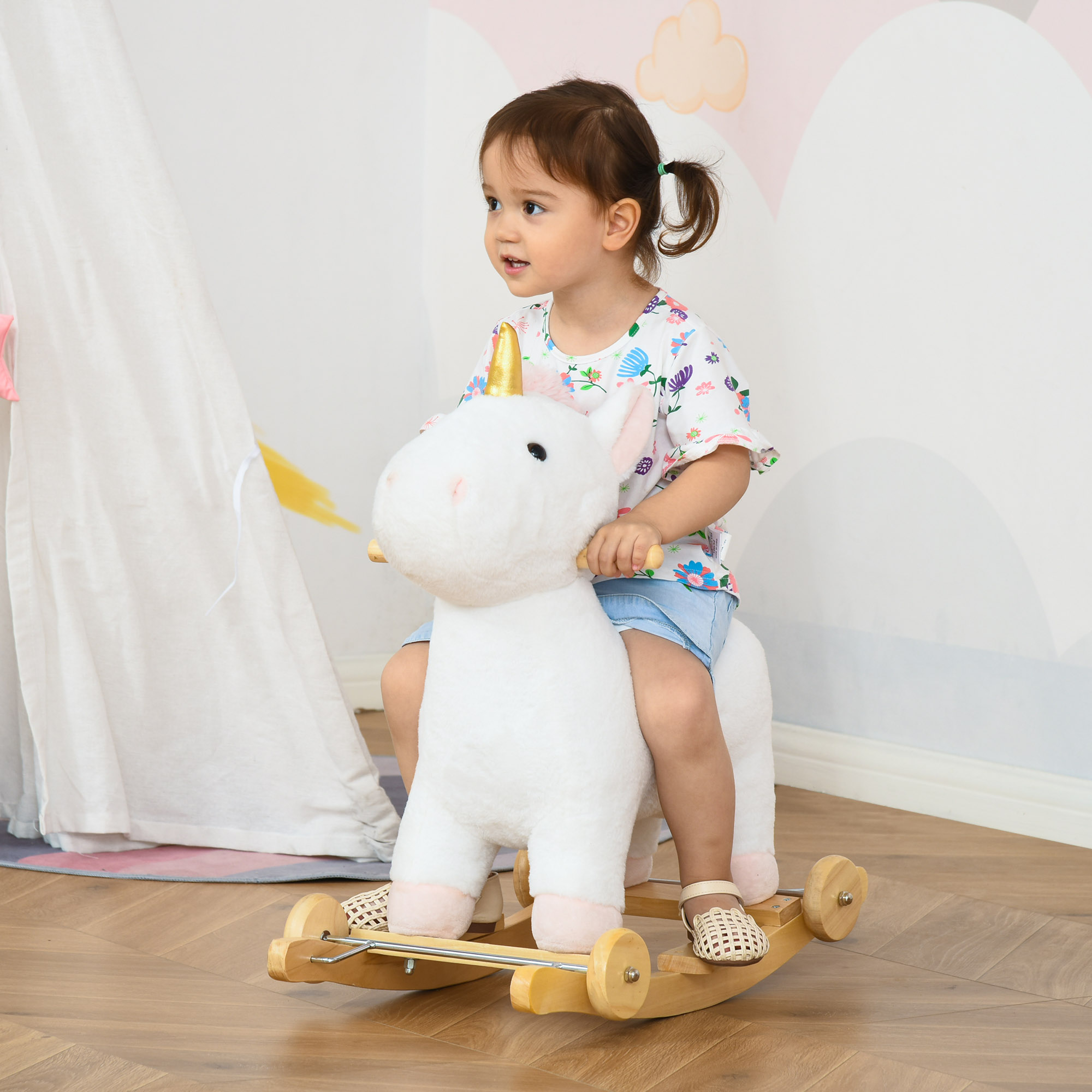 Una bambina cavalca un unicorno a dondolo di peluche bianco in una stanza luminosa.