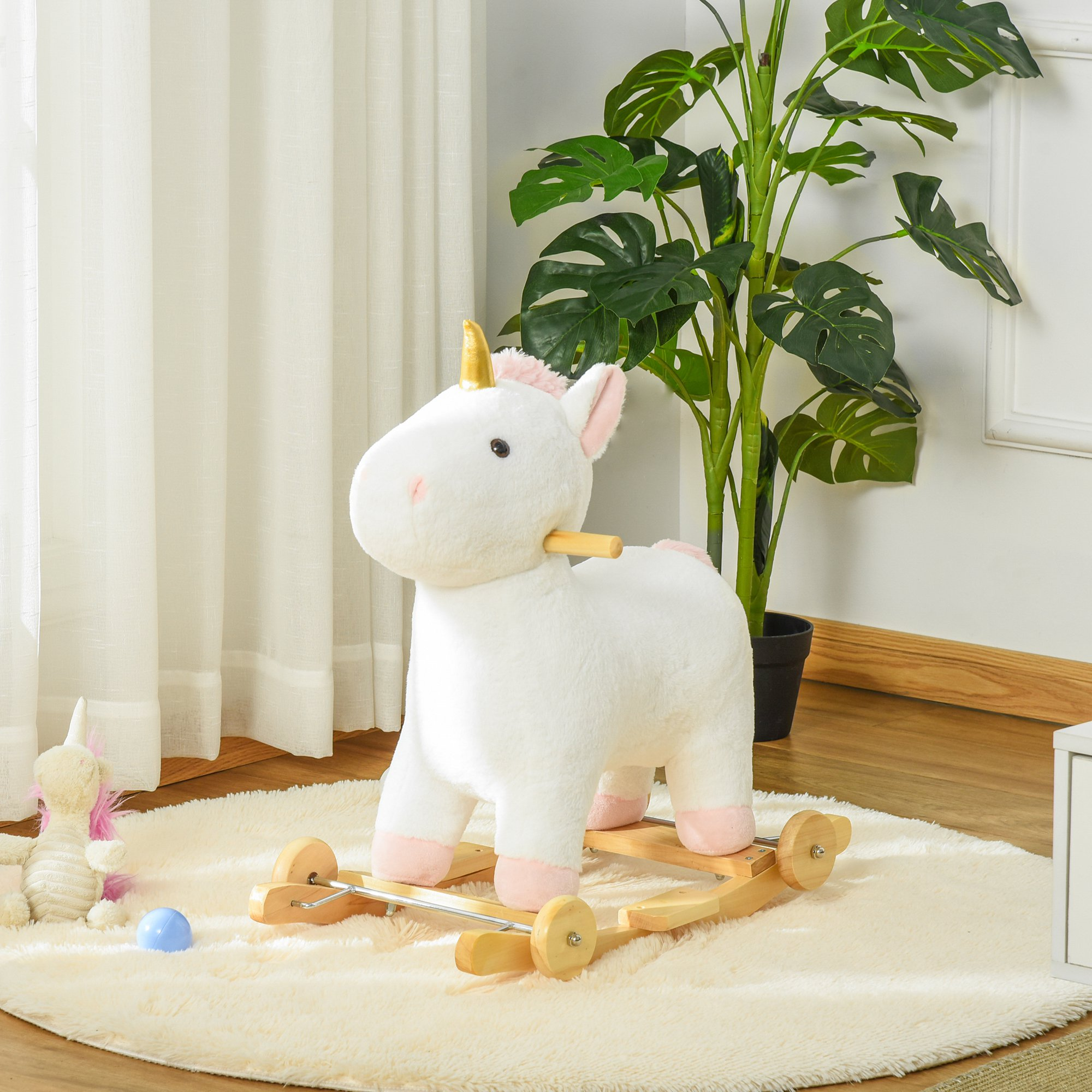 Un dondolo a forma di unicorno bianco di peluche su un tappeto vicino a una pianta.