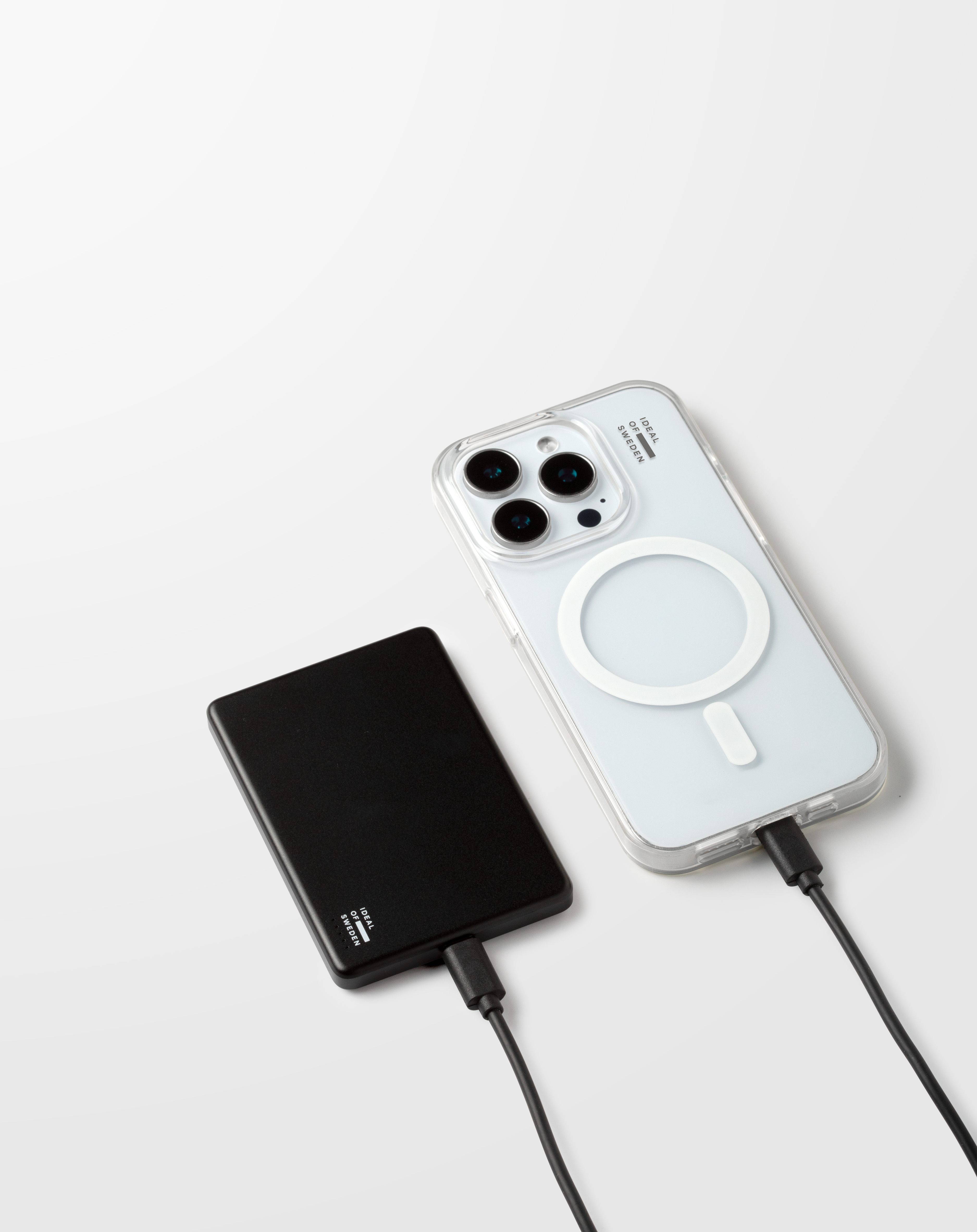 Un smartphone dans une coque et une batterie externe reposent sur une surface blanche, reliés par des câbles.
