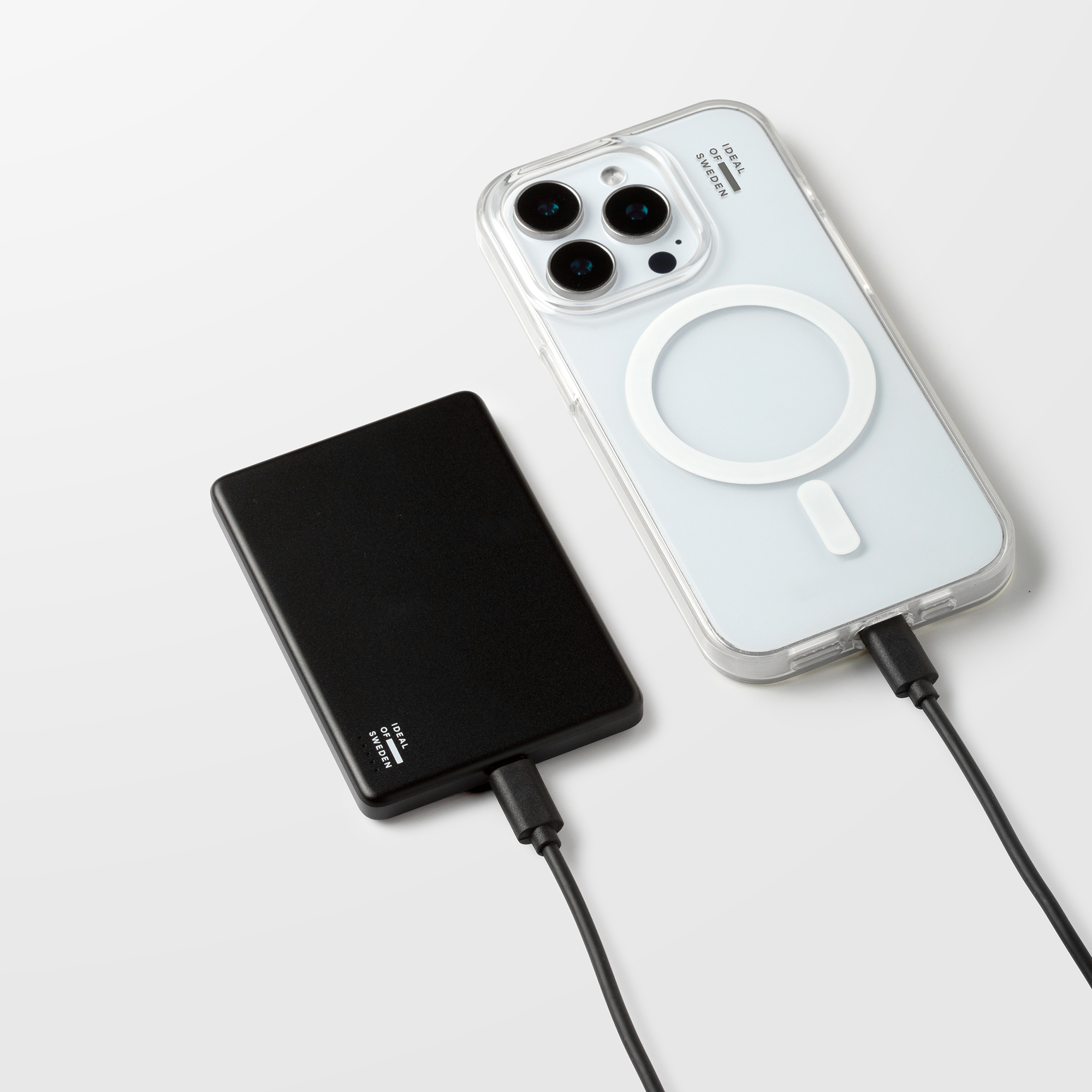 Une batterie externe noire et un smartphone dans une coque avec un câble de charge connecté sur fond blanc.