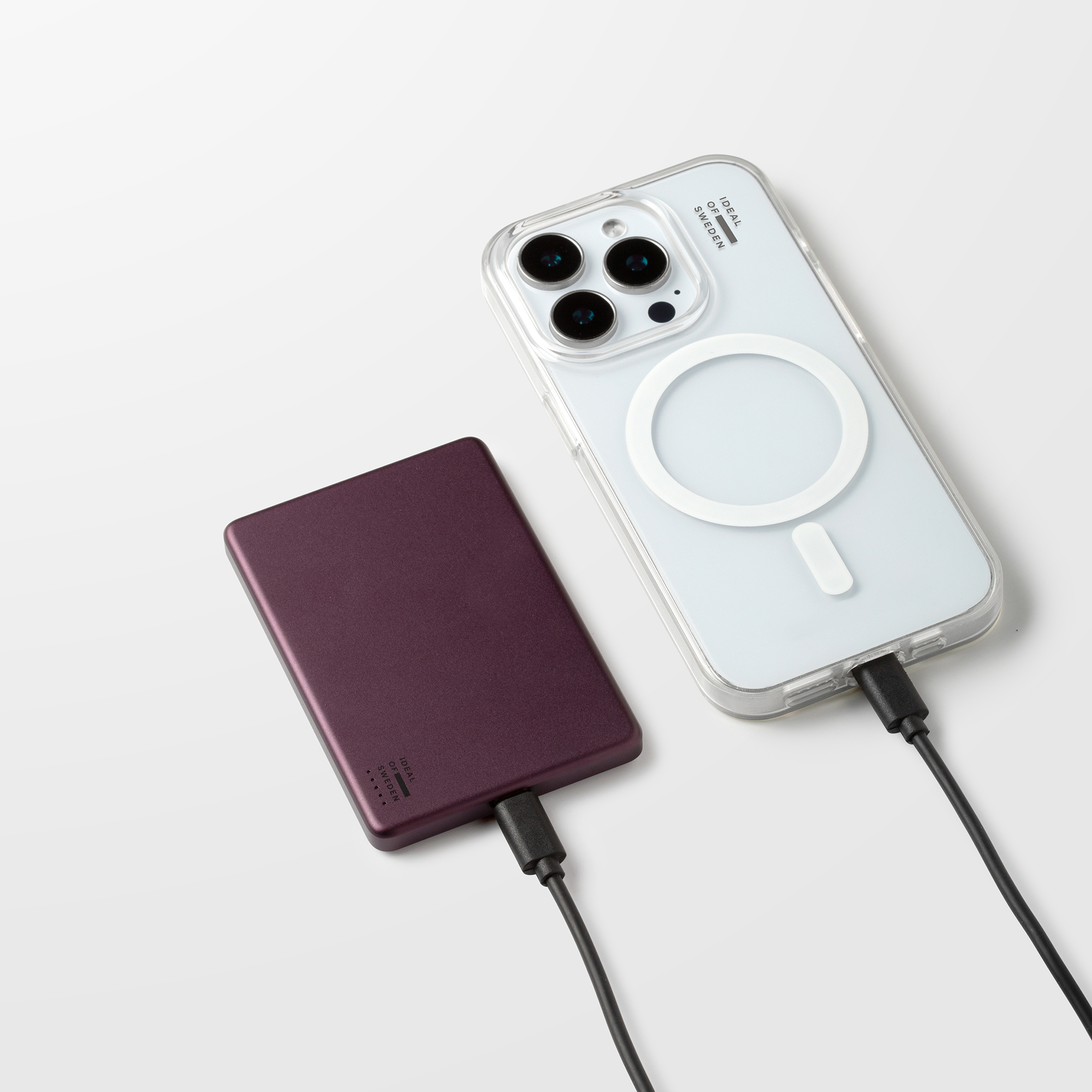 Une batterie externe rouge foncé et un smartphone dans une coque transparente avec câbles sur fond blanc.