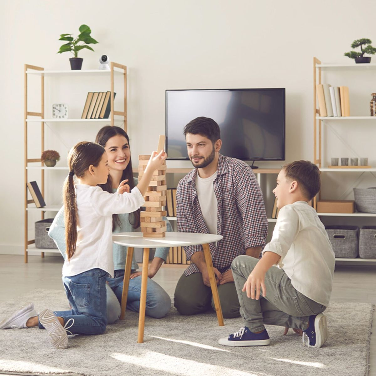 Eine Familie spielt gemeinsam Jenga im Wohnzimmer mit TV und Regalen.