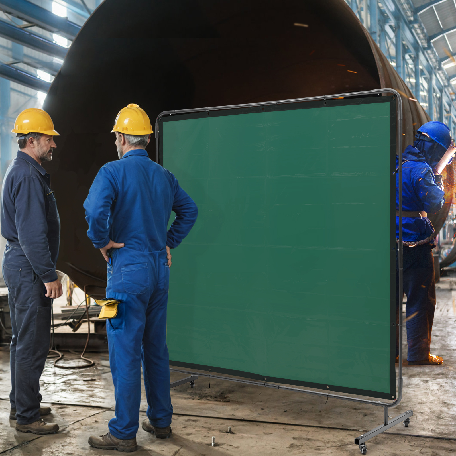 Dos trabajadores con overoles azules y cascos amarillos junto a una pantalla verde en una fábrica.