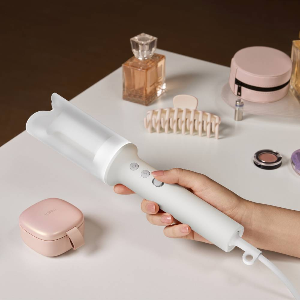 Une main tient un appareil coiffant blanc sur une table avec des cosmétiques.