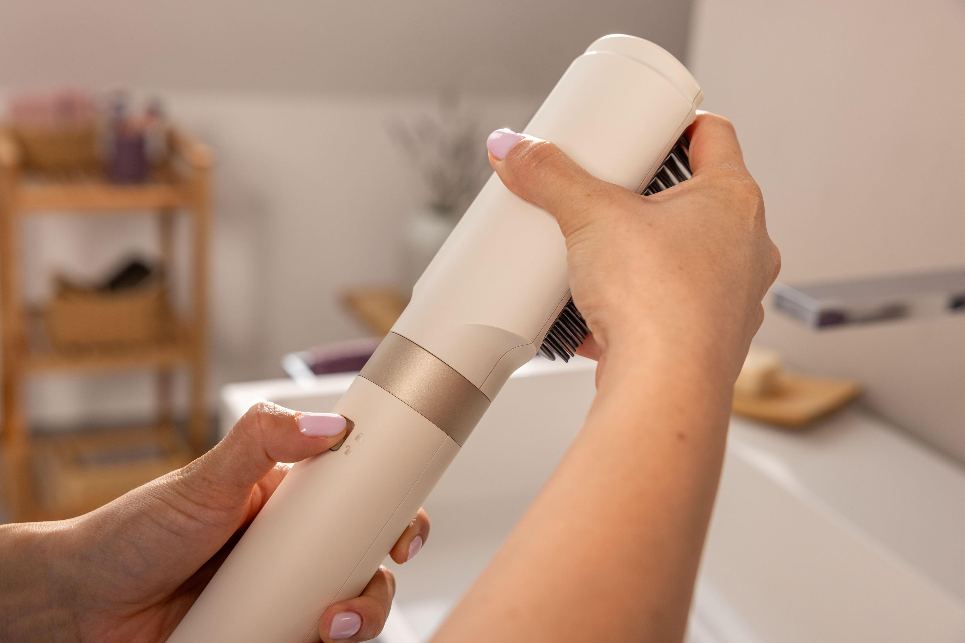 Persona che tiene in mano una spazzola per capelli bianca e dorata, in un bagno luminoso.