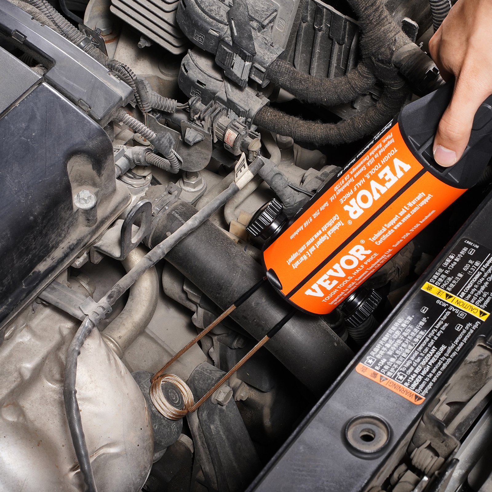 Mano sostiene un dispositivo Vevor naranja con una bobina de cable insertada en un motor de auto.