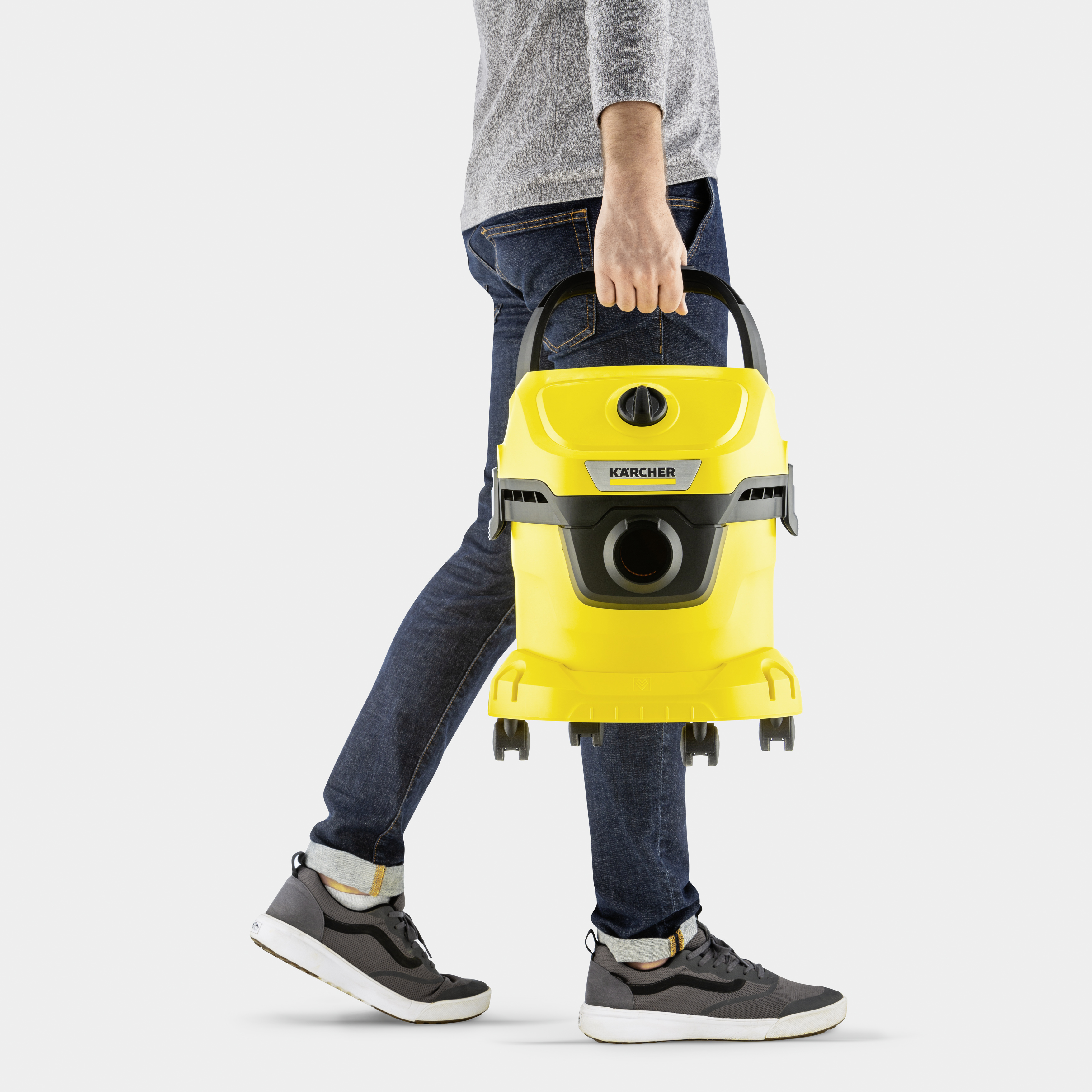 Una persona in jeans e camicia grigia trasporta un aspirapolvere Karcher giallo.