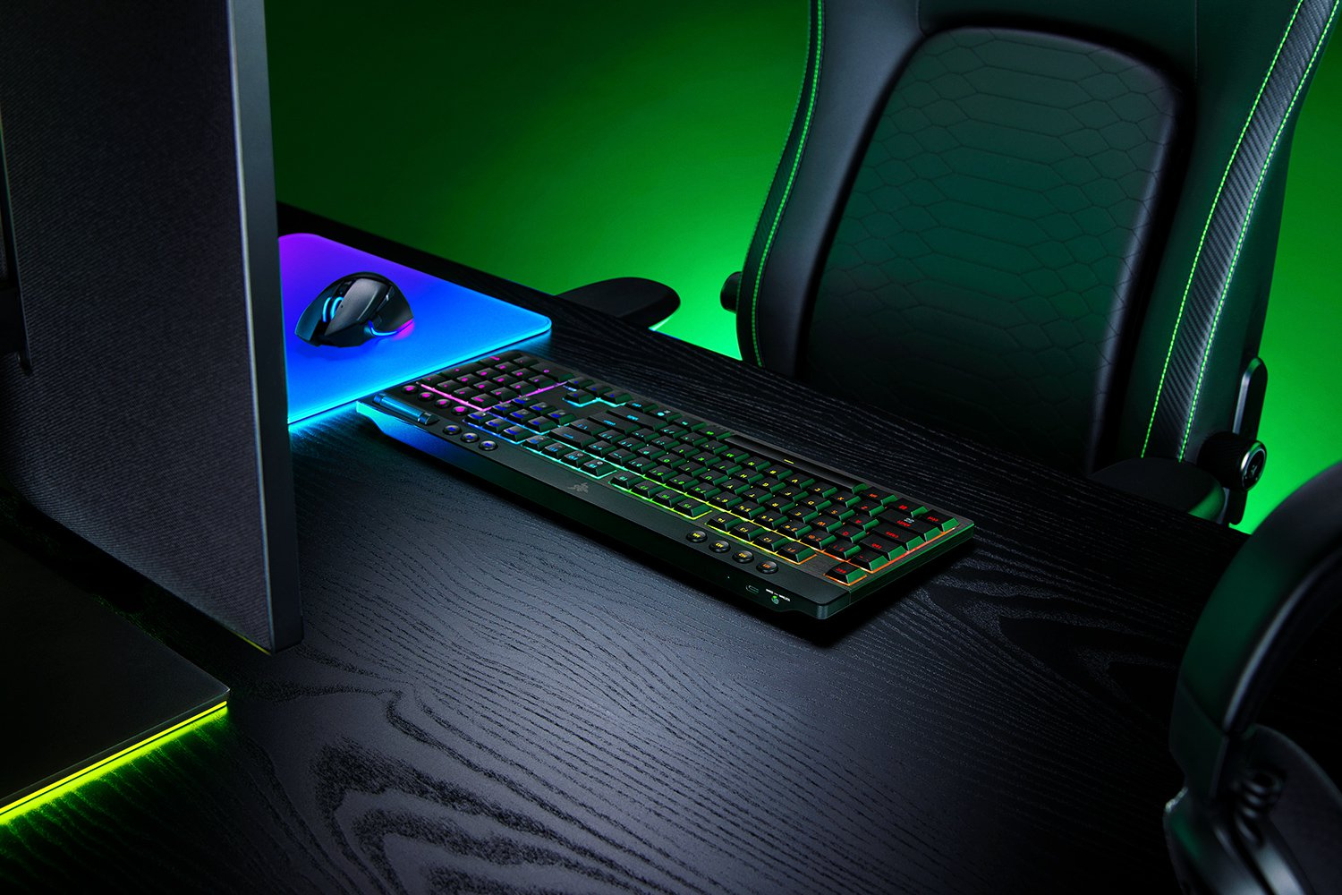 Postazione da gioco con tastiera RGB, mouse, monitor e sedia su sfondo verde.