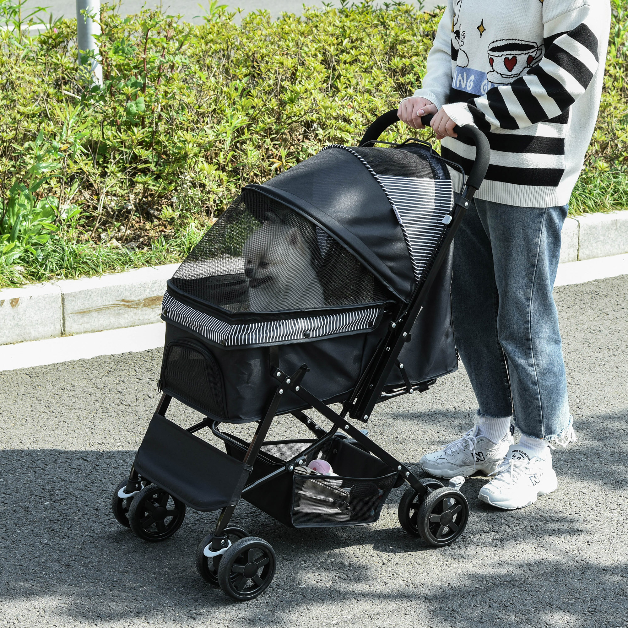 Una persona con un maglione a righe spinge un passeggino nero per animali con un cane all'interno.