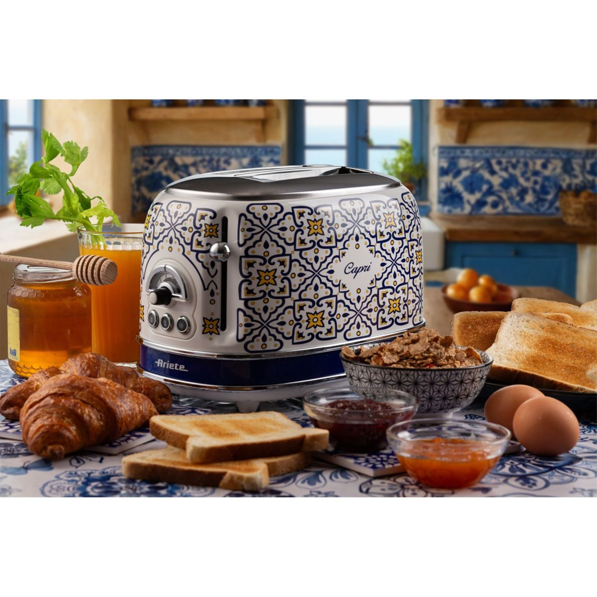 Ein blau-weiß gemusterter Toaster steht auf einem Tisch mit Toast, Croissants, Eiern, Müslischalen und Säften in einer Küche.