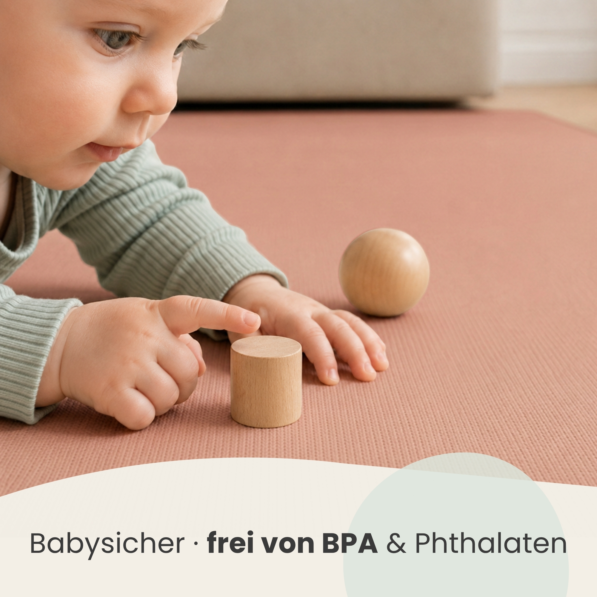 Ein Baby in grüner Kleidung spielt mit Holzspielzeug auf einer rosa Matte.
