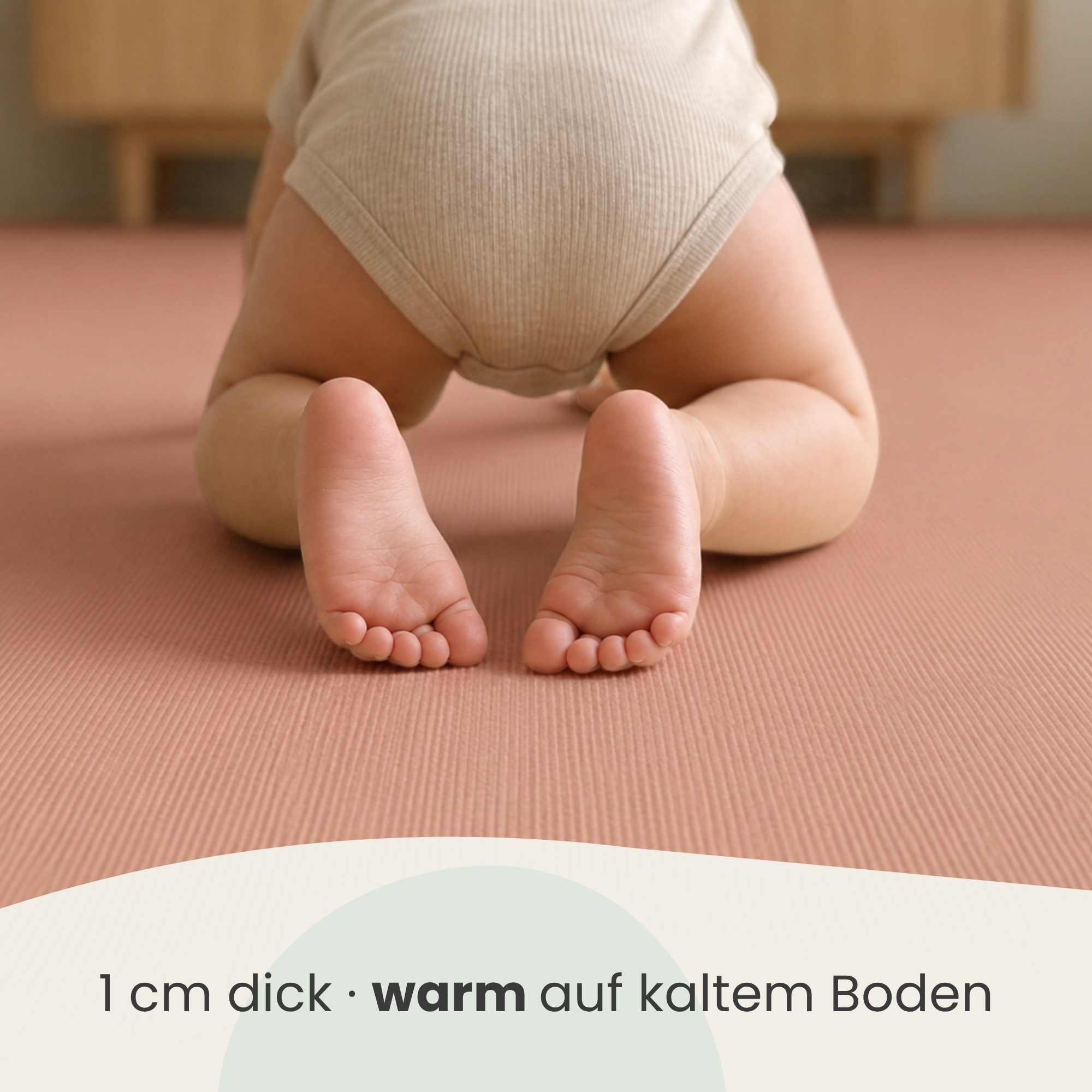 Ein Baby im beigen Body krabbelt auf einer rosa Spielmatte, von hinten gesehen.