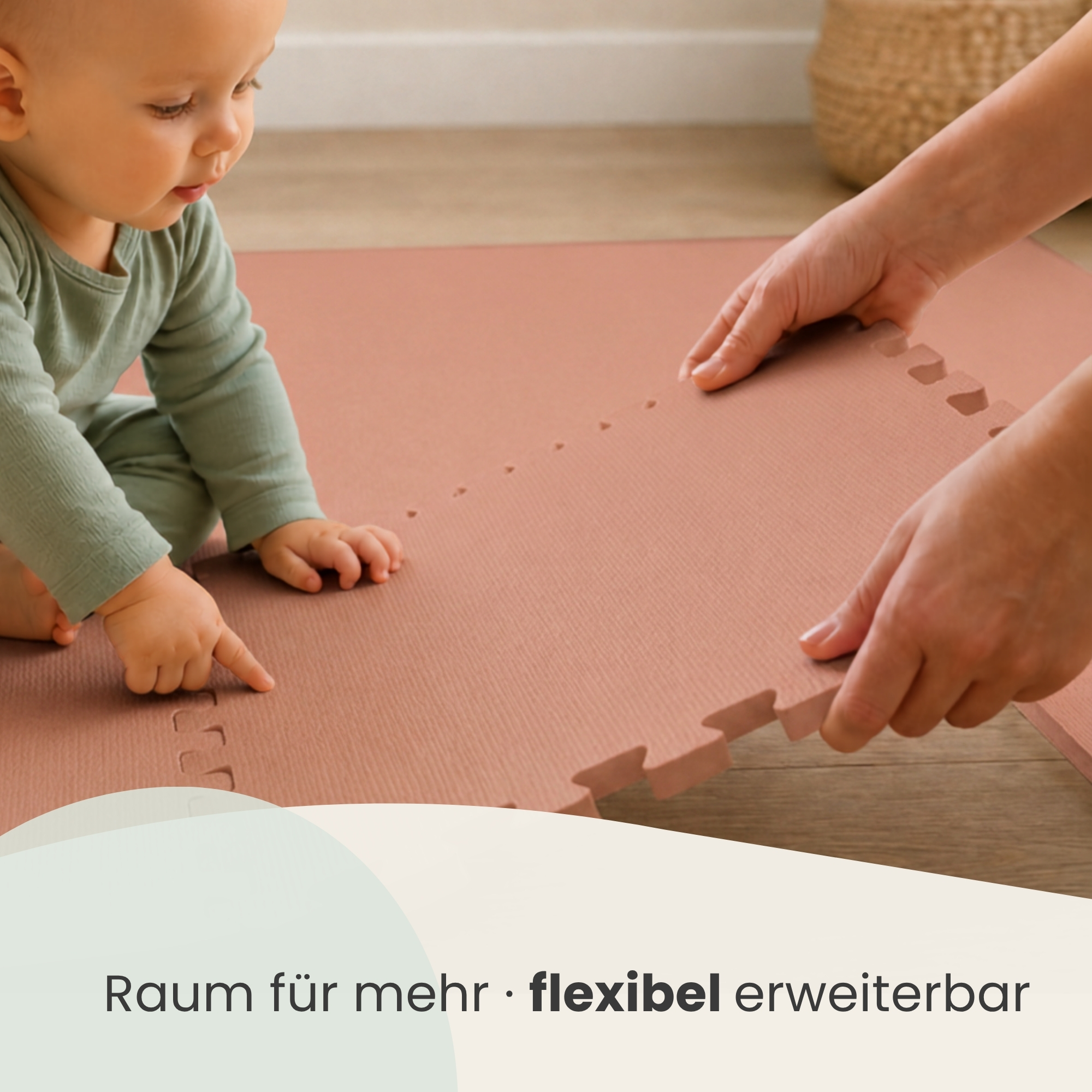 Ein Baby im grünen Strampler schaut zu, wie Hände eine rosa Schaumstoff-Spielmatte auf dem Holzfußboden zusammenfügen.