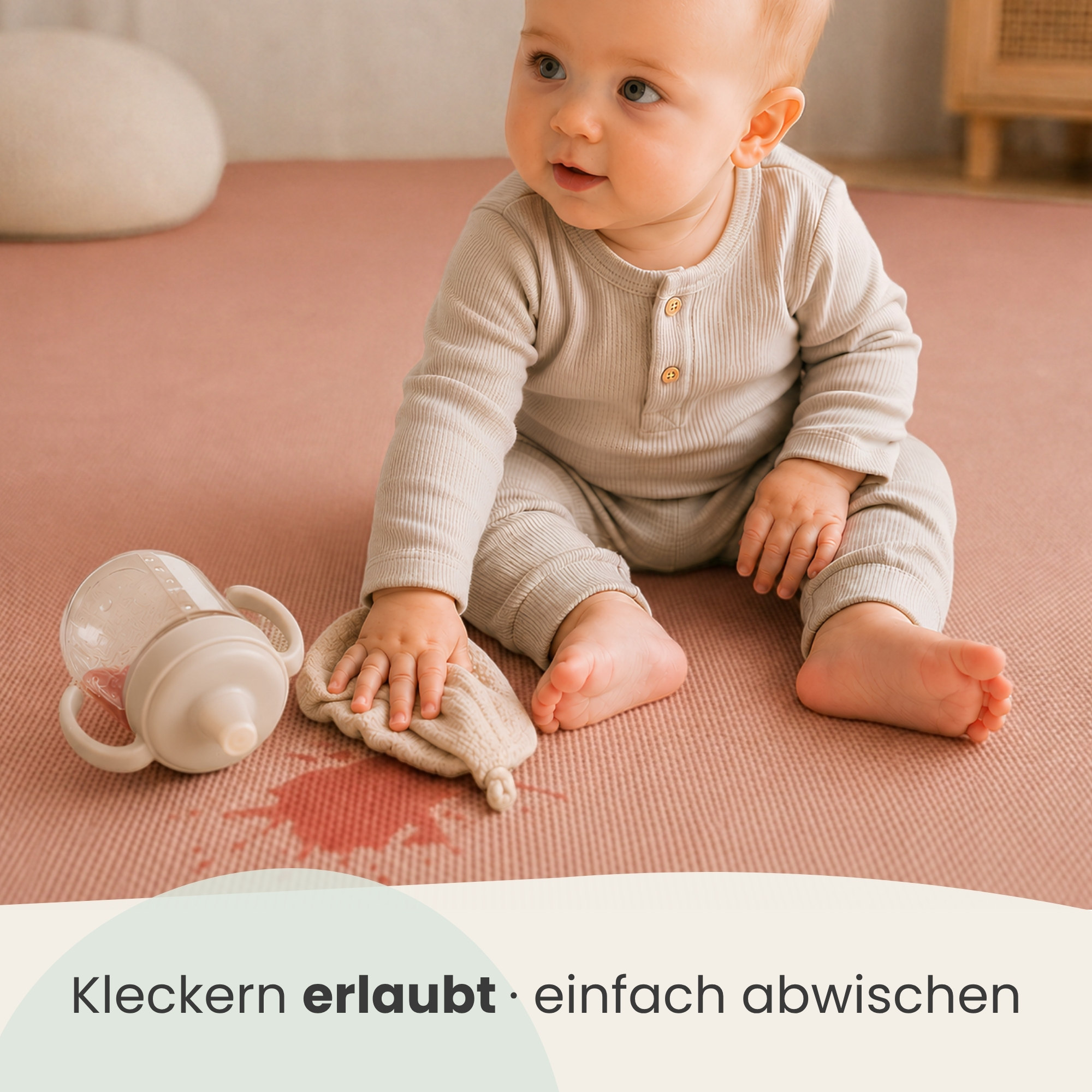 Baby in beiger Kleidung sitzt auf einer rosafarbenen Matte neben einer Trinkflasche und wischt einen Fleck weg.
