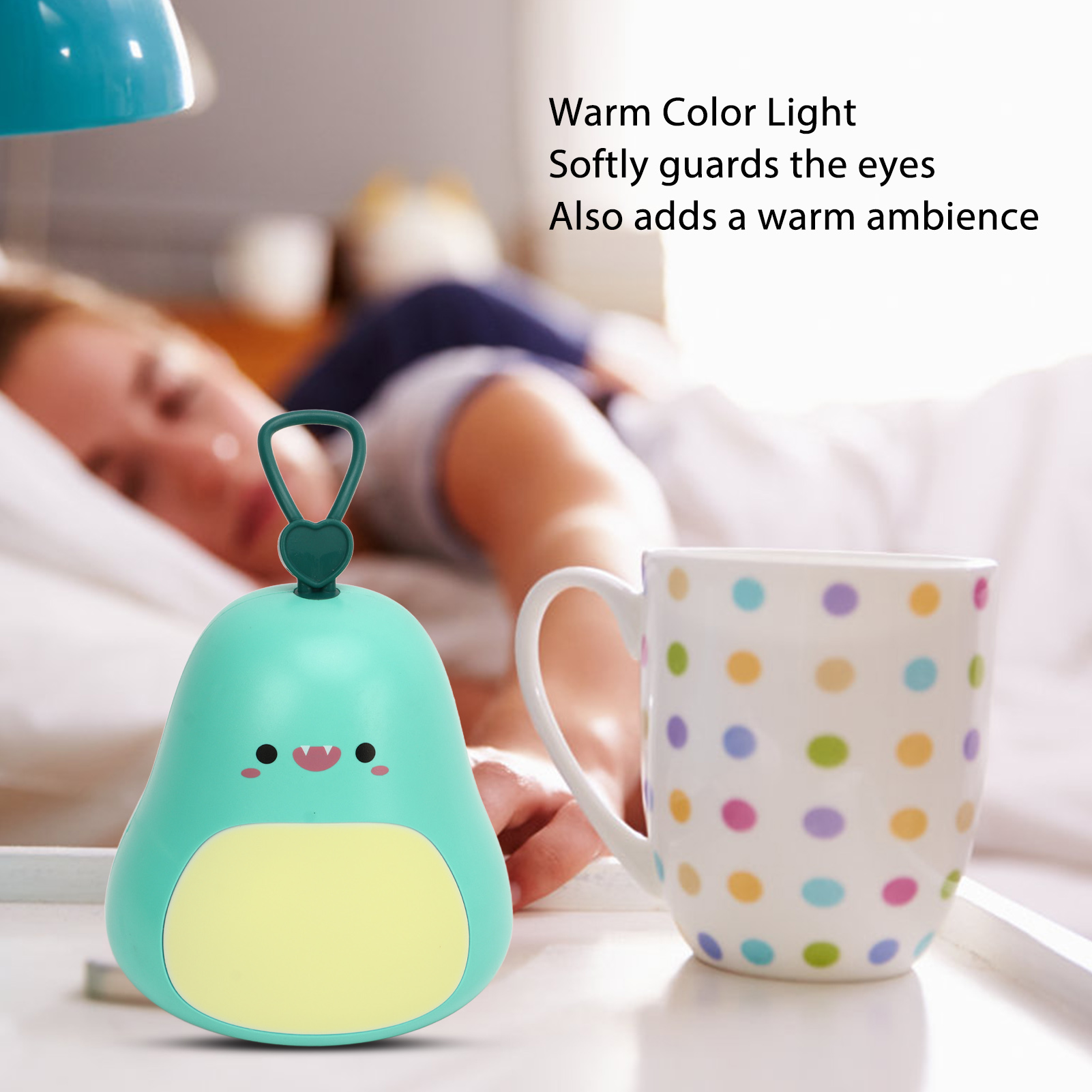 Eine süße grüne Lampe in Dinosaurierform und ein Tasse mit Punkten stehen auf einer weißen Oberfläche, dahinter eine schlafende Person.