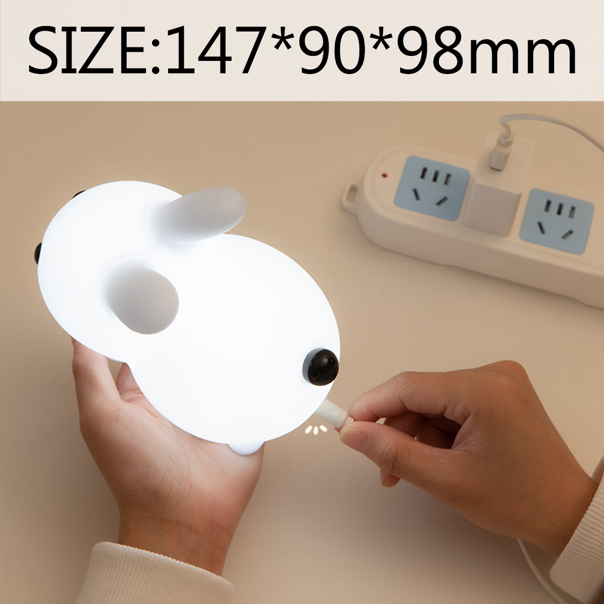Eine Hand verbindet ein Ladekabel mit einer weißen Tier-Nachtlampe mit Maßen von 147x90x98mm.