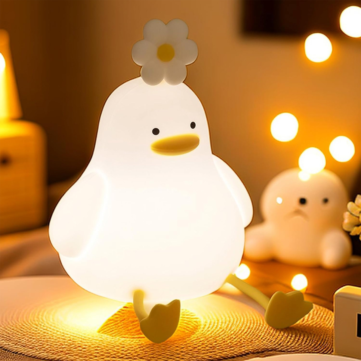 Eine süße, weiße Entenlampe mit einer Blume auf dem Kopf sitzt auf einem Tisch, umgeben von warmen Lichtern.
