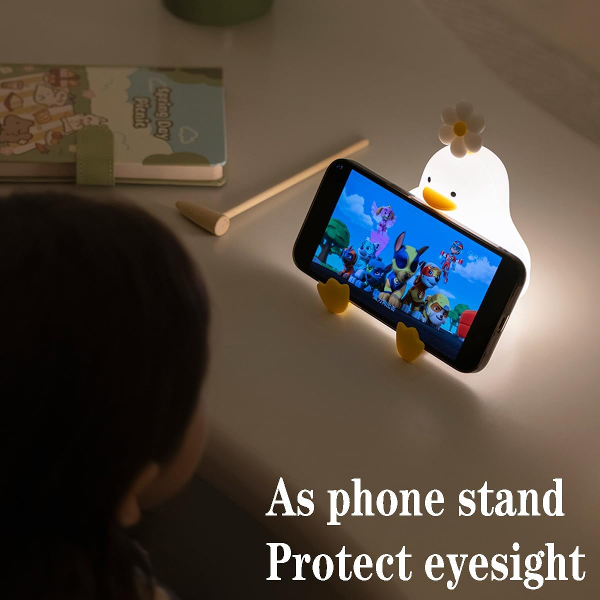 Ein Kind schaut auf ein Smartphone, das in einer gelben Enten-Lampe mit Ständer steckt.