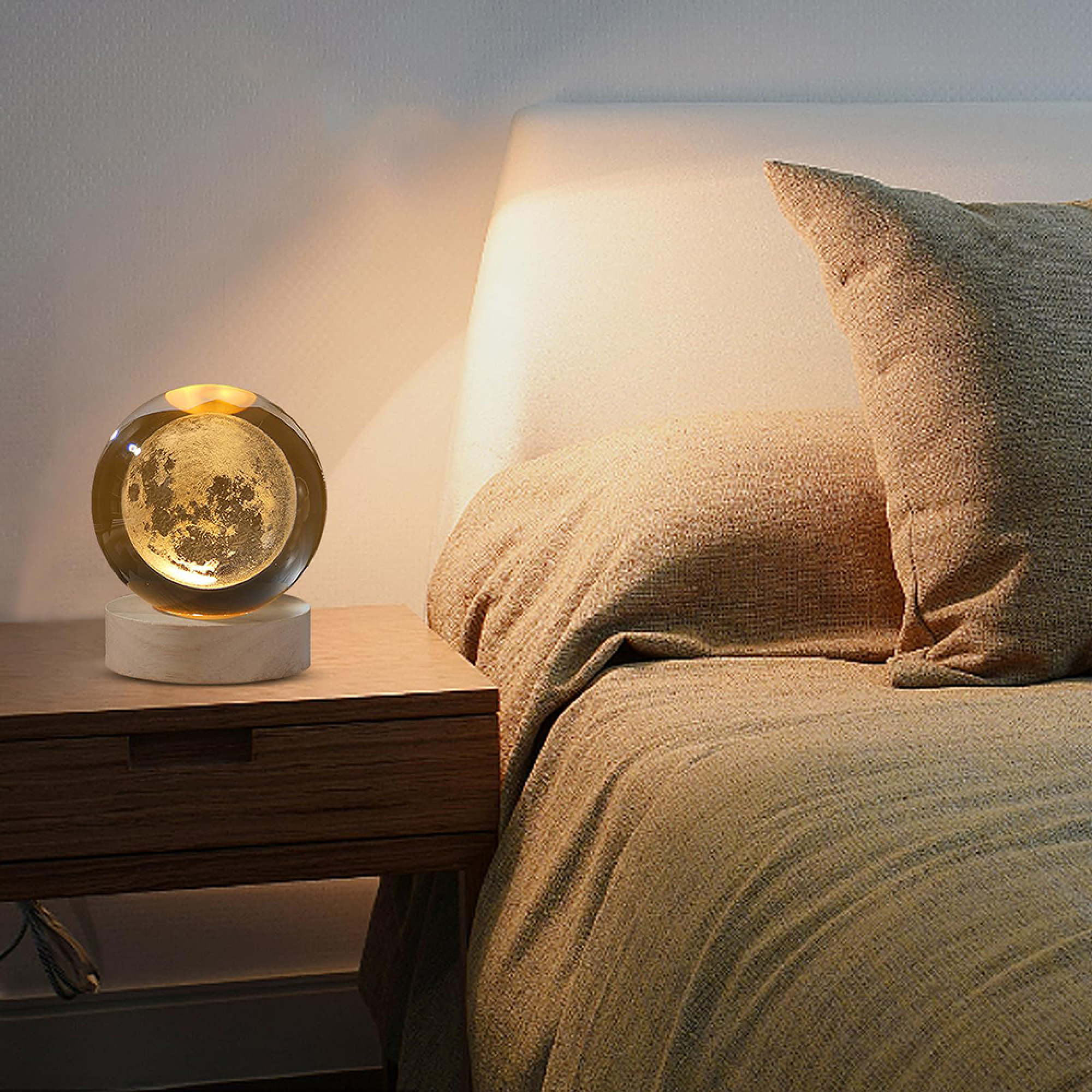 Eine glühende Mondlampe auf einem Nachttisch neben einem Bett mit brauner Bettwäsche.