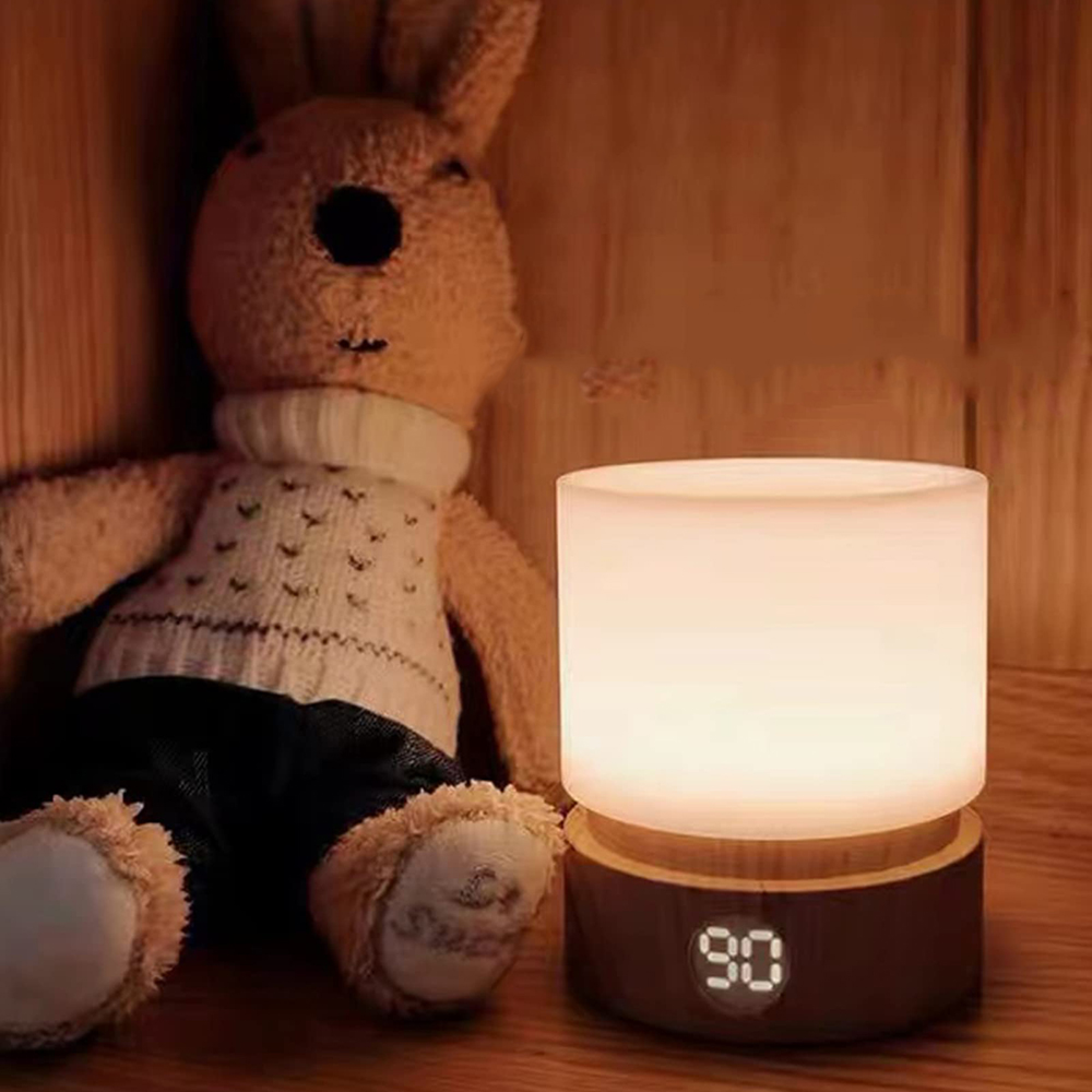 Ein Kuschelhase sitzt neben einer beleuchteten Tischlampe mit Holzsokel auf einem Holztisch.