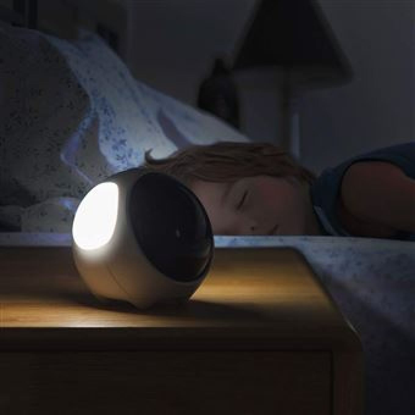 Ein Kind schläft in einem Bett, während ein kugelförmiges Nachtlicht auf dem Nachttisch sanft leuchtet.