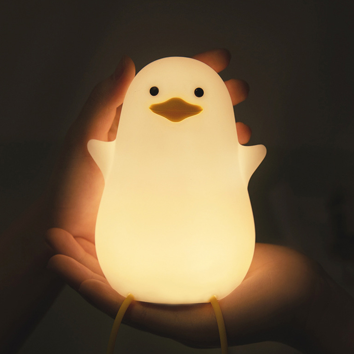 Eine Hand hält eine kleine, leuchtende, ente-förmige Lampe mit schwarzen Augen und gelbem Schnabel.