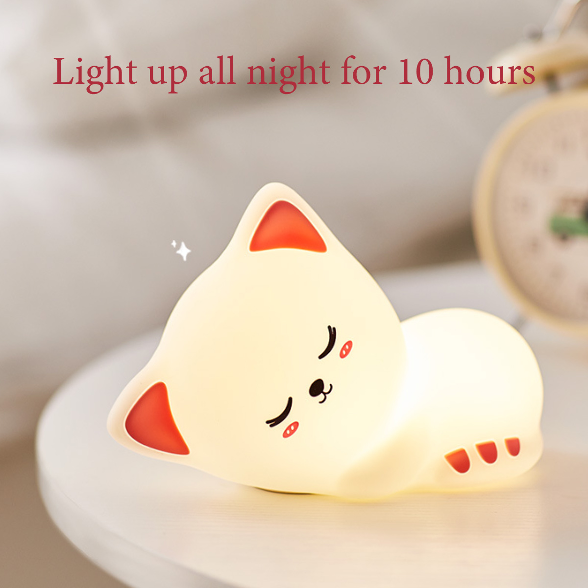 Ein weißes, katzenförmiges Nachtlicht leuchtet auf einem weißen Tisch, mit einem Wecker im Hintergrund.